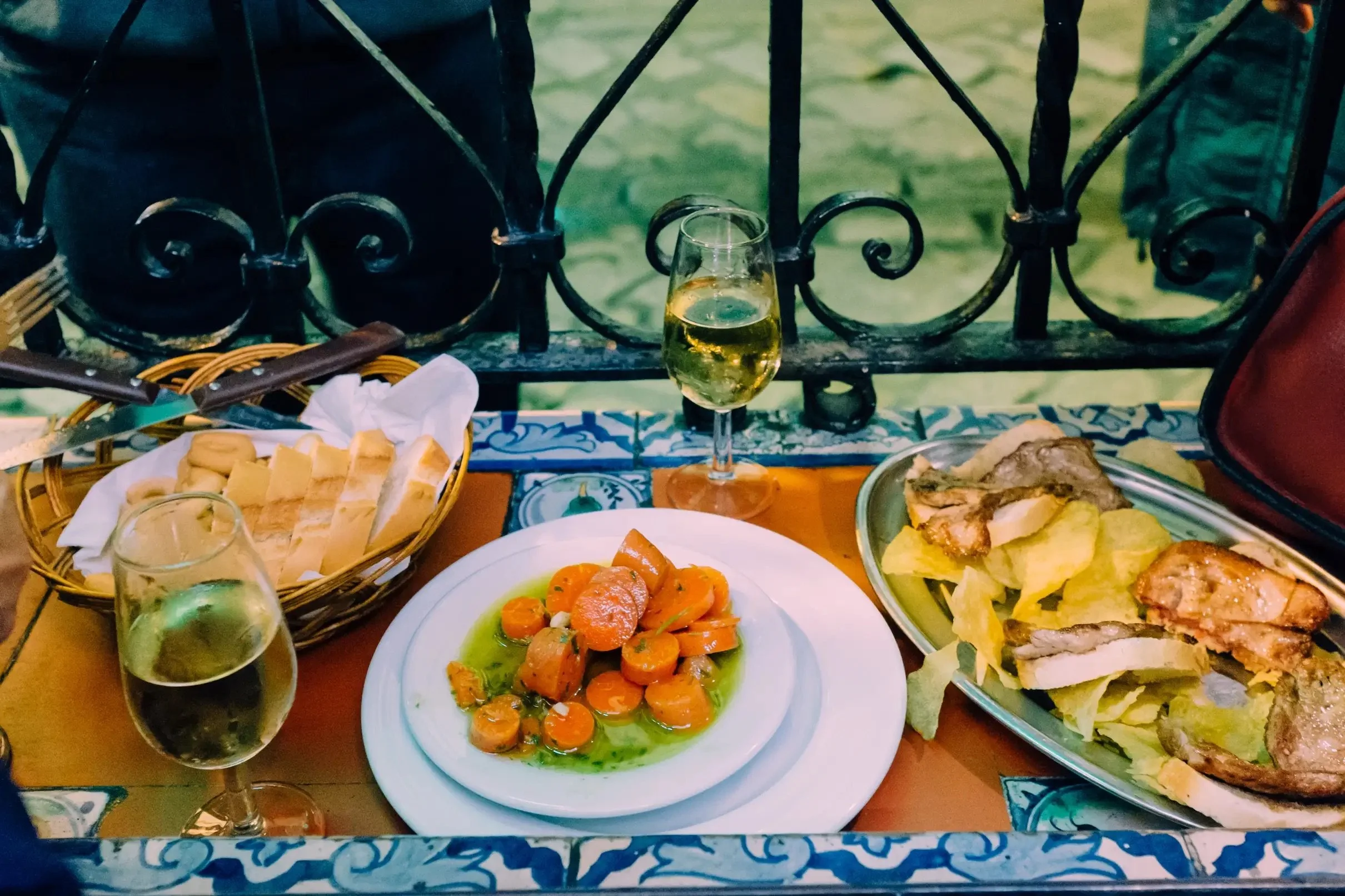 Tapas tradicionales sevillanas con vino blanco en una terraza del centro de Sevilla, incluyendo zanahorias aliñadas, pescado y pan en una experiencia gastronómica andaluza.