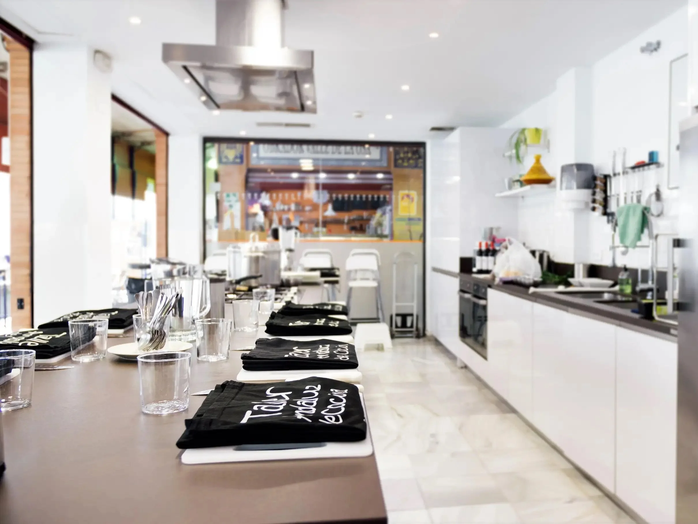 Cocina profesional preparada para una clase de cocina en Sevilla, con estaciones individuales equipadas y espacio moderno junto a un mercado local.