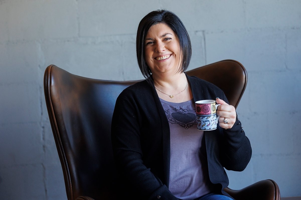 Krystal Thorhaug, co-founder of Undercover Creators, smiling while holding a coffee mug, sitting in a brown leather chair against a plain gray wall.