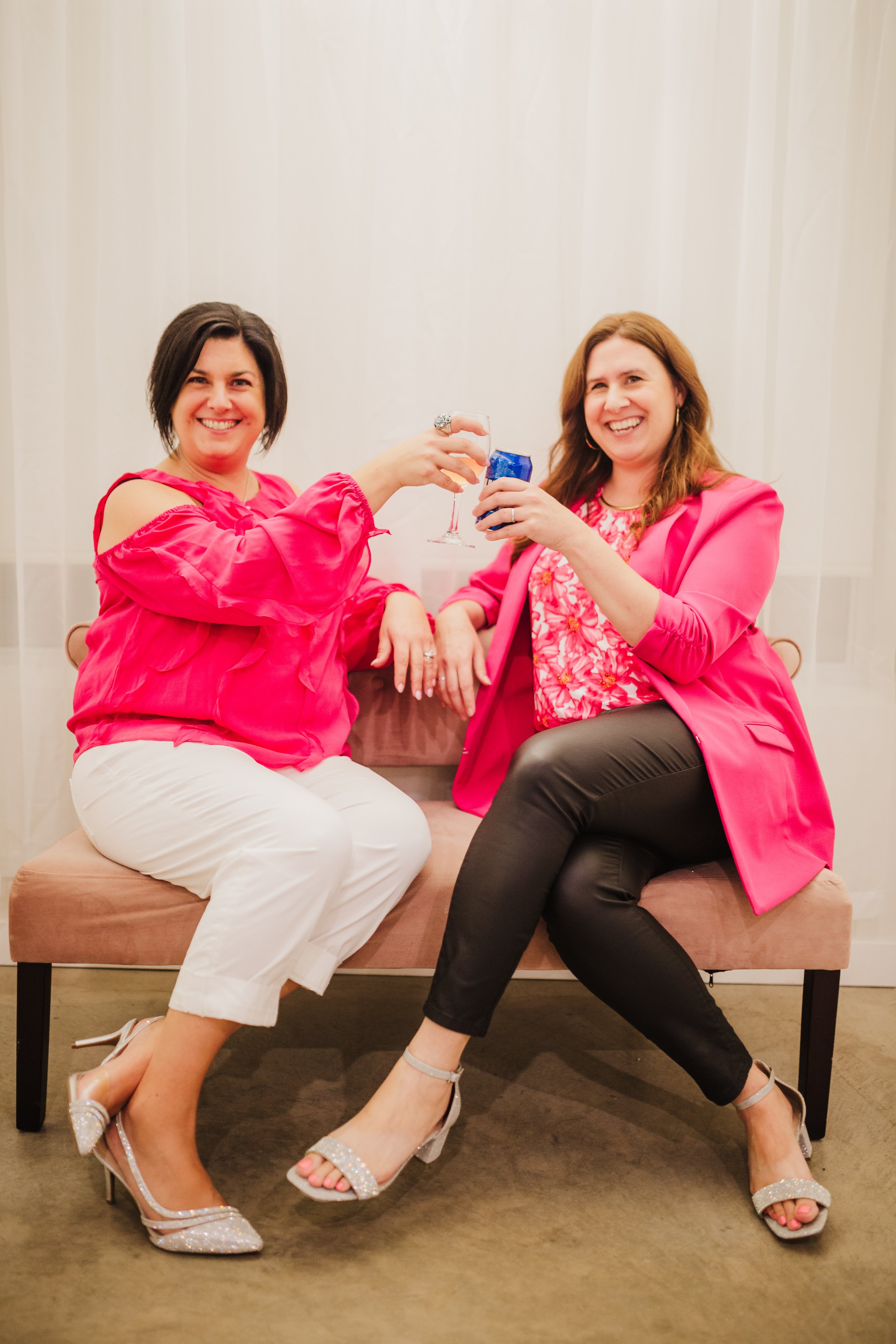 Krystal Thorhaug and Lindsay Fuchs, the female founders of Undercover Creators, sitting together on a pink bench, toasting drinks and smiling, showing a celebratory and personable brand culture.