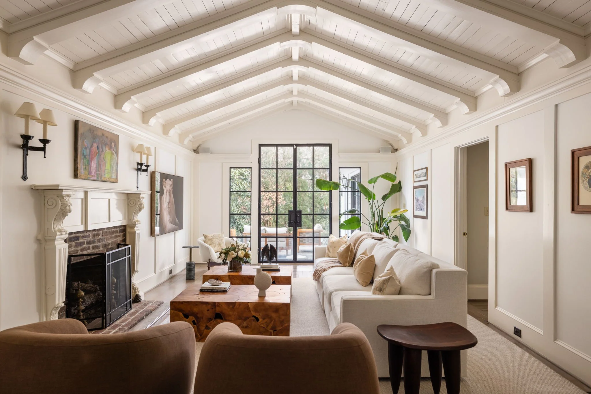 A large living room showcases a unique vaulted ceiling with wood beams, modern furnishings, and black steel doors.