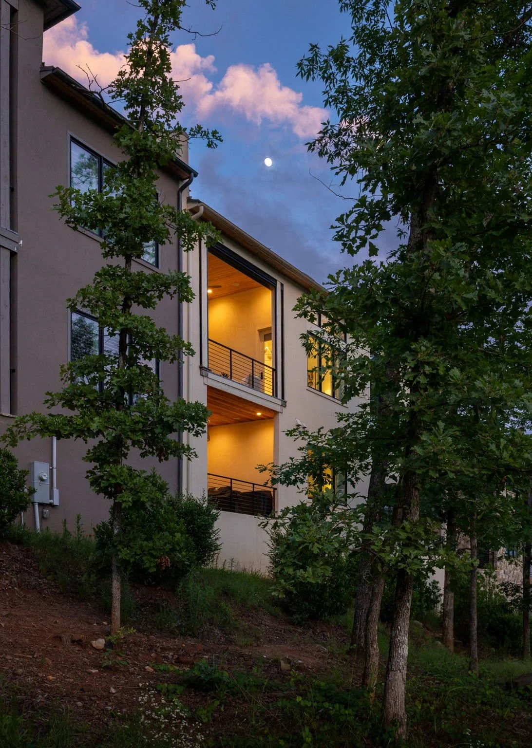 Hillside townhouse photographed at dusk with a view of the moon and an arch of pink clouds.