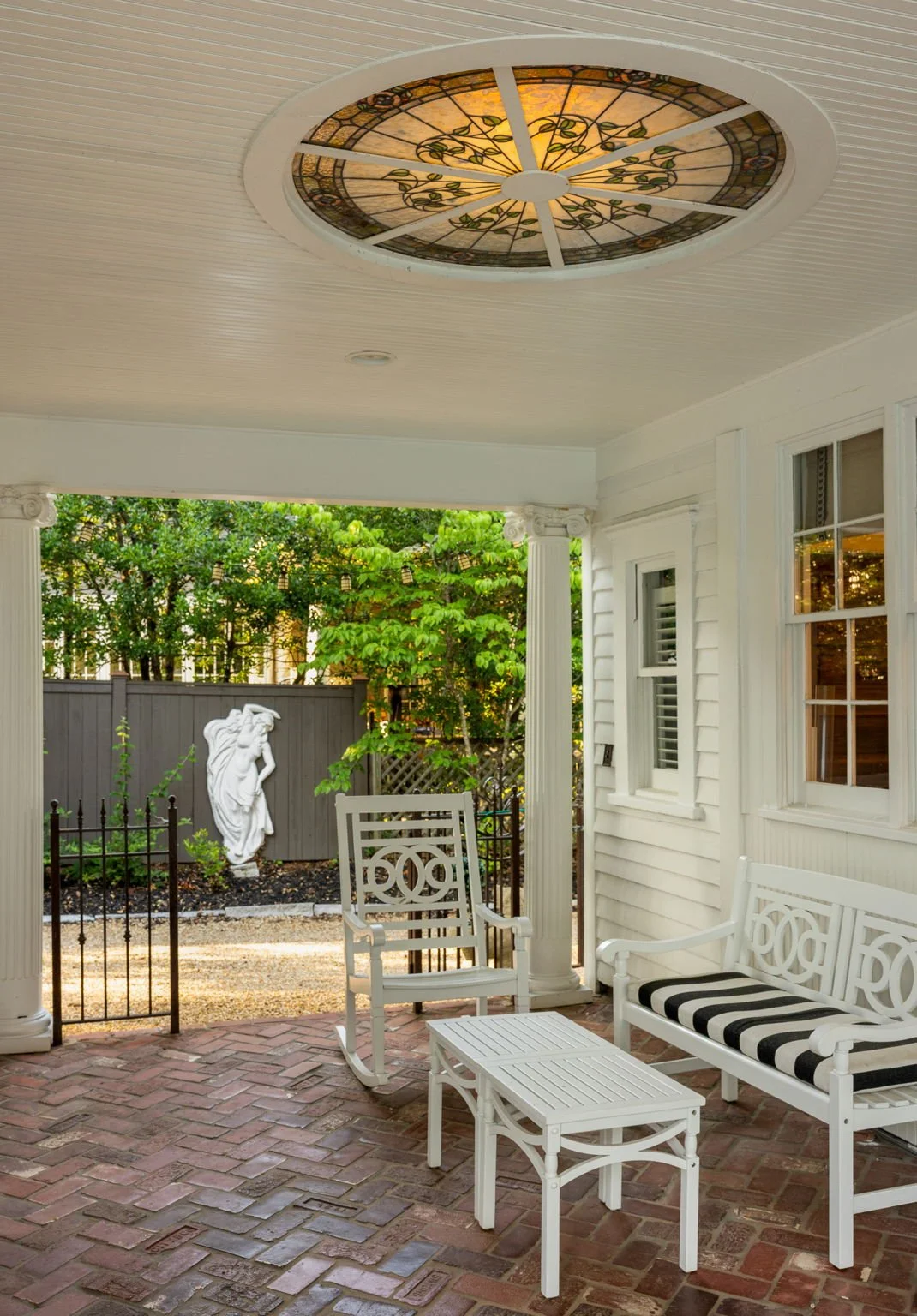 Stained glass above and herringbone brick below in a seating area, with a white garden sculpture.