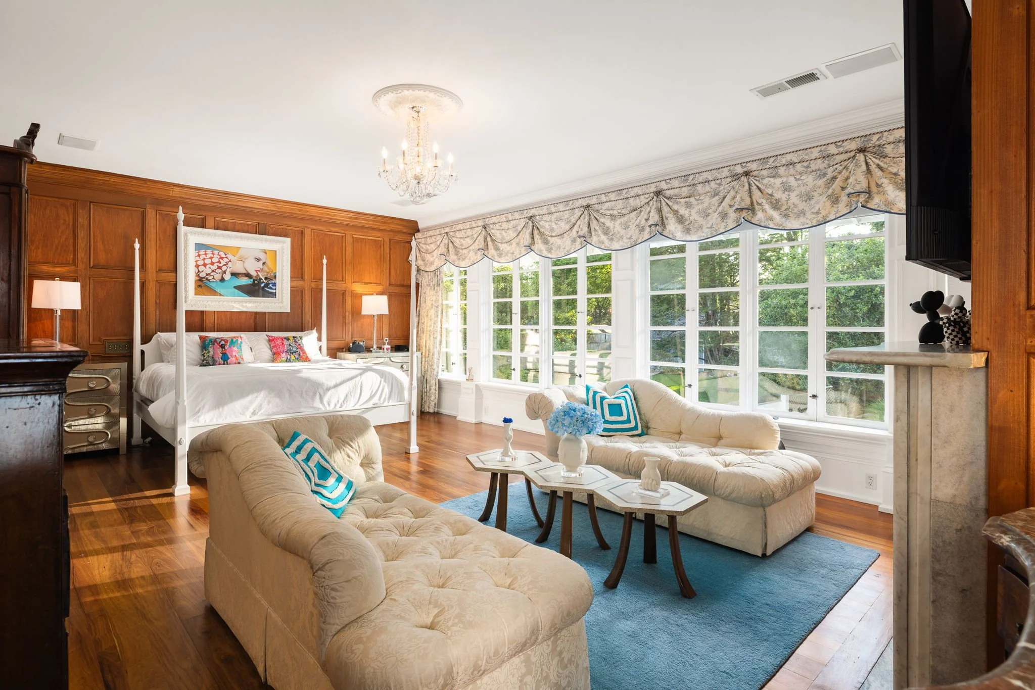 A primary bedroom clad in wood paneling blends antique furniture with modern art and fixtures.