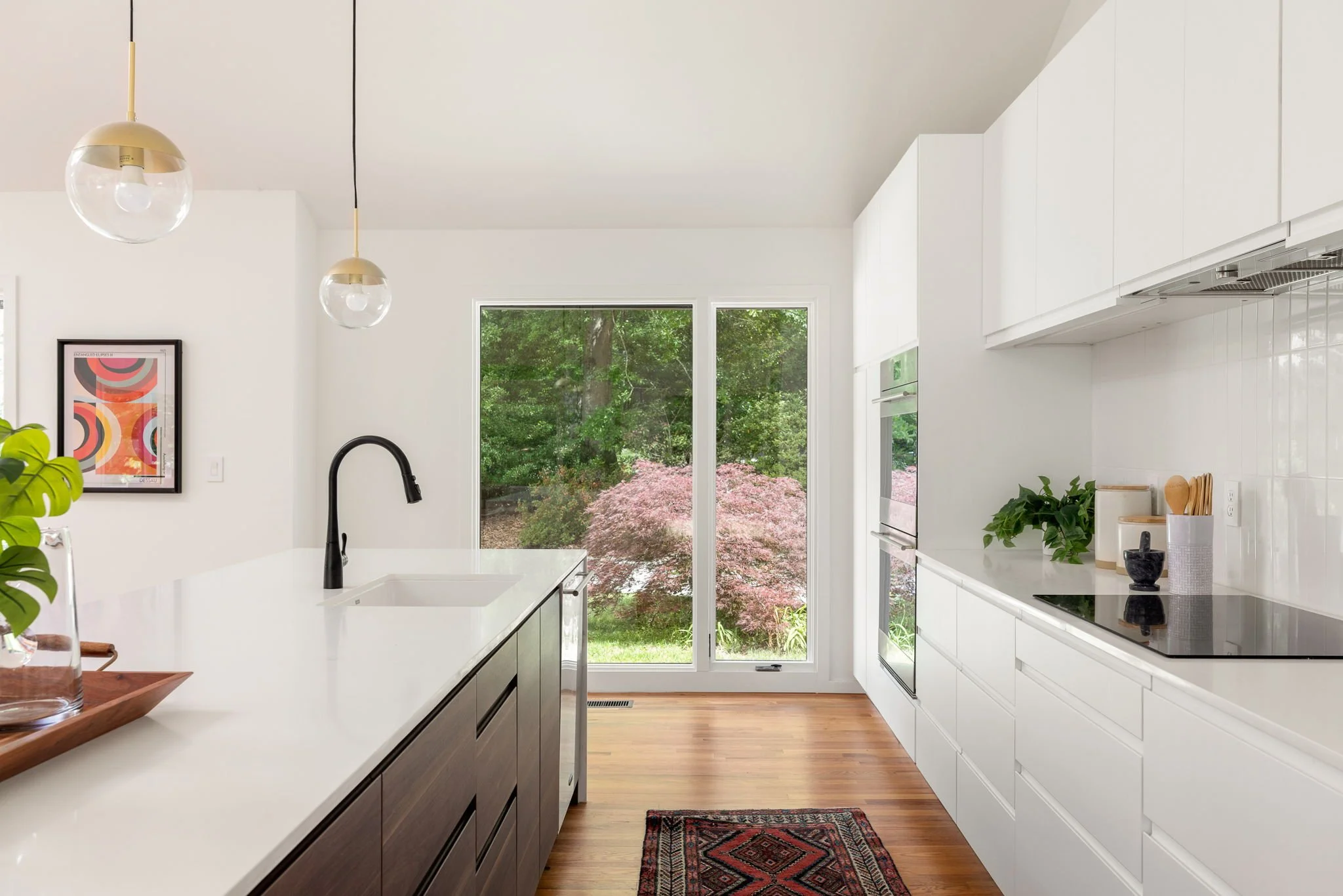 A white modern kitchen with colorful landscaping outside a large viewing window.