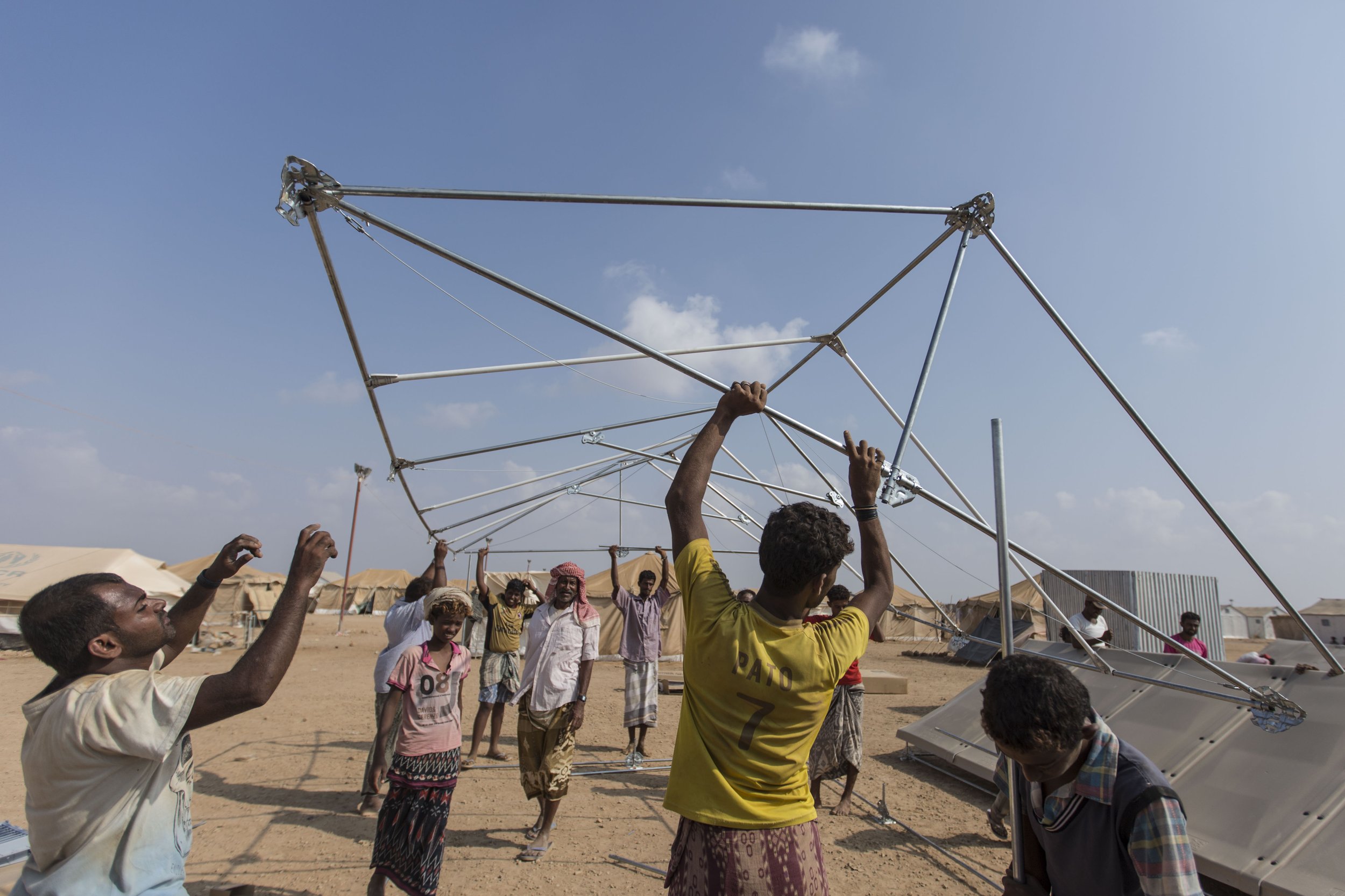 Refugees receive incentive payments for the work they do at the camp. Here, a group puts up a shelter which will be used as a community centre.