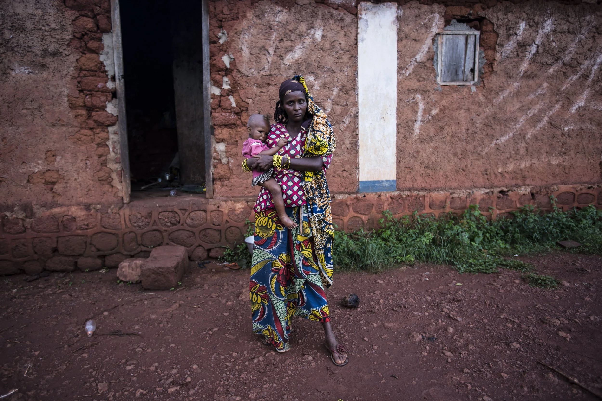Halima, Moussa's wife, outside her Yaloke shelter holding her 2 years old Rachida. The mother's anxiety has been on the rise due to noticeably deteriorating health condition of the infant after one year in the enclave.