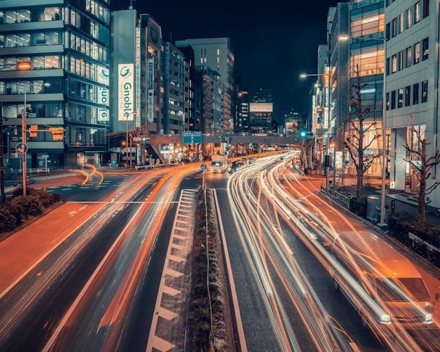 Aerial view of roads at night, illuminated by streetlights and vehicle headlights, creating a vibrant and dynamic urban scene.