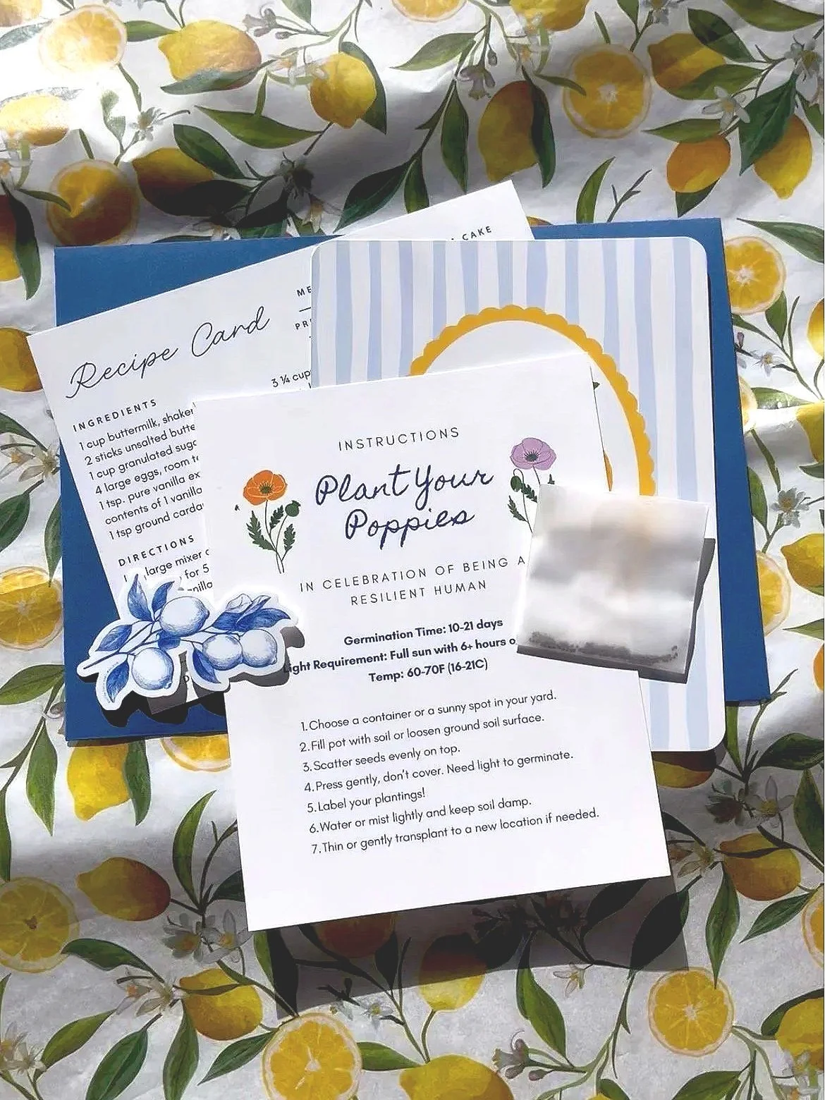 A collection of gardening and recipe cards laid out on a lemon-themed tablecloth, including instructions for planting poppies and a lemon cake recipe.