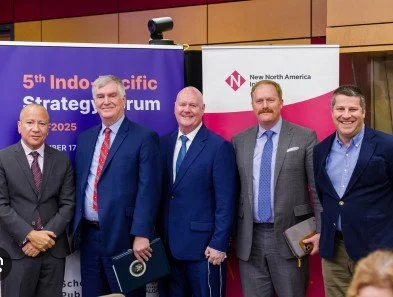 Five men wearing suits who participated on a panel discussion posing for a photo in front of a few promotional signs.