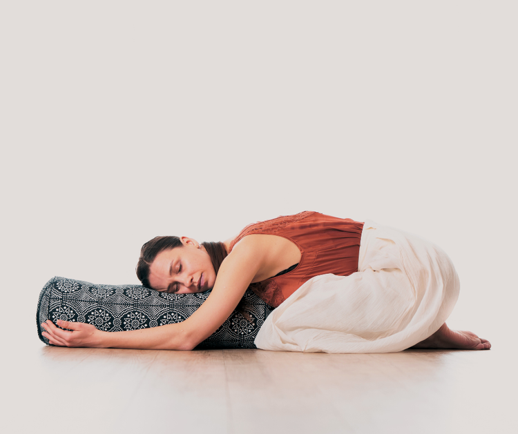 A practitioner resting in a supported restorative yoga pose with bolsters to promote deep physical and mental rest.