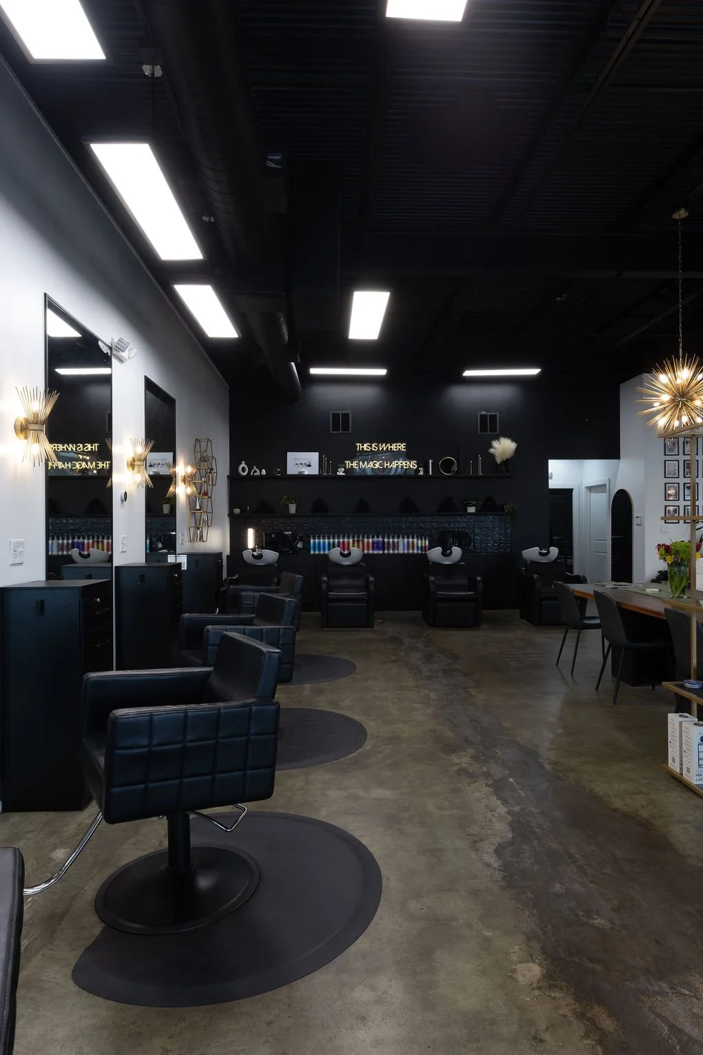 Interior of a modern hair salon with black and white decor, black salon chairs, and washbasins at the back.