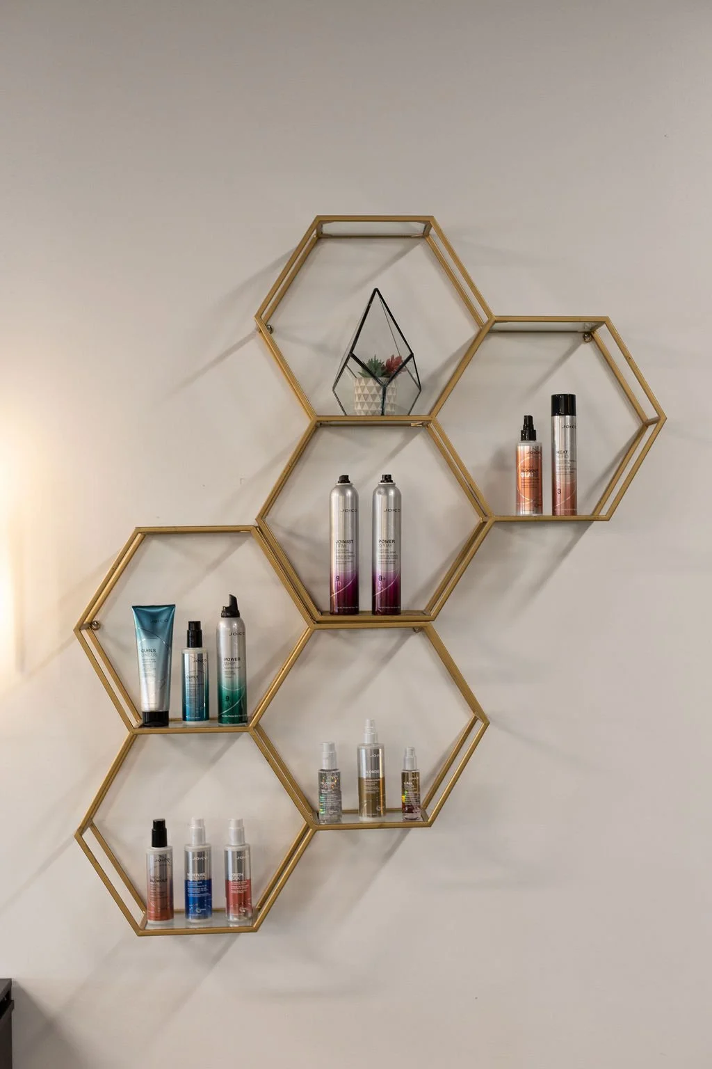 Wall-mounted hexagonal shelves with hair care products and a decorative terrarium.