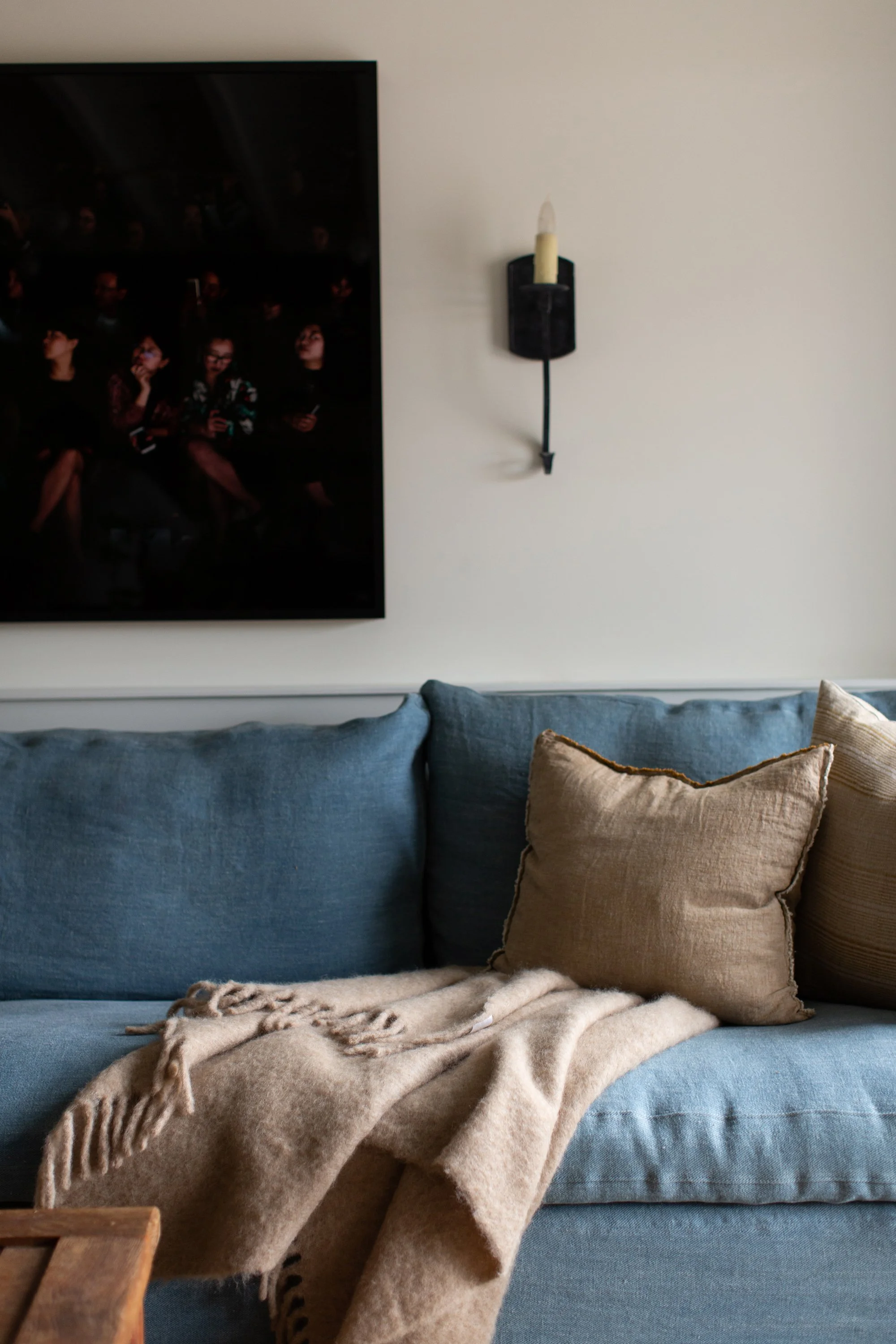 Living room sofa closeup, showing throw pillows and blanket, artwork on wall and wall sconce.