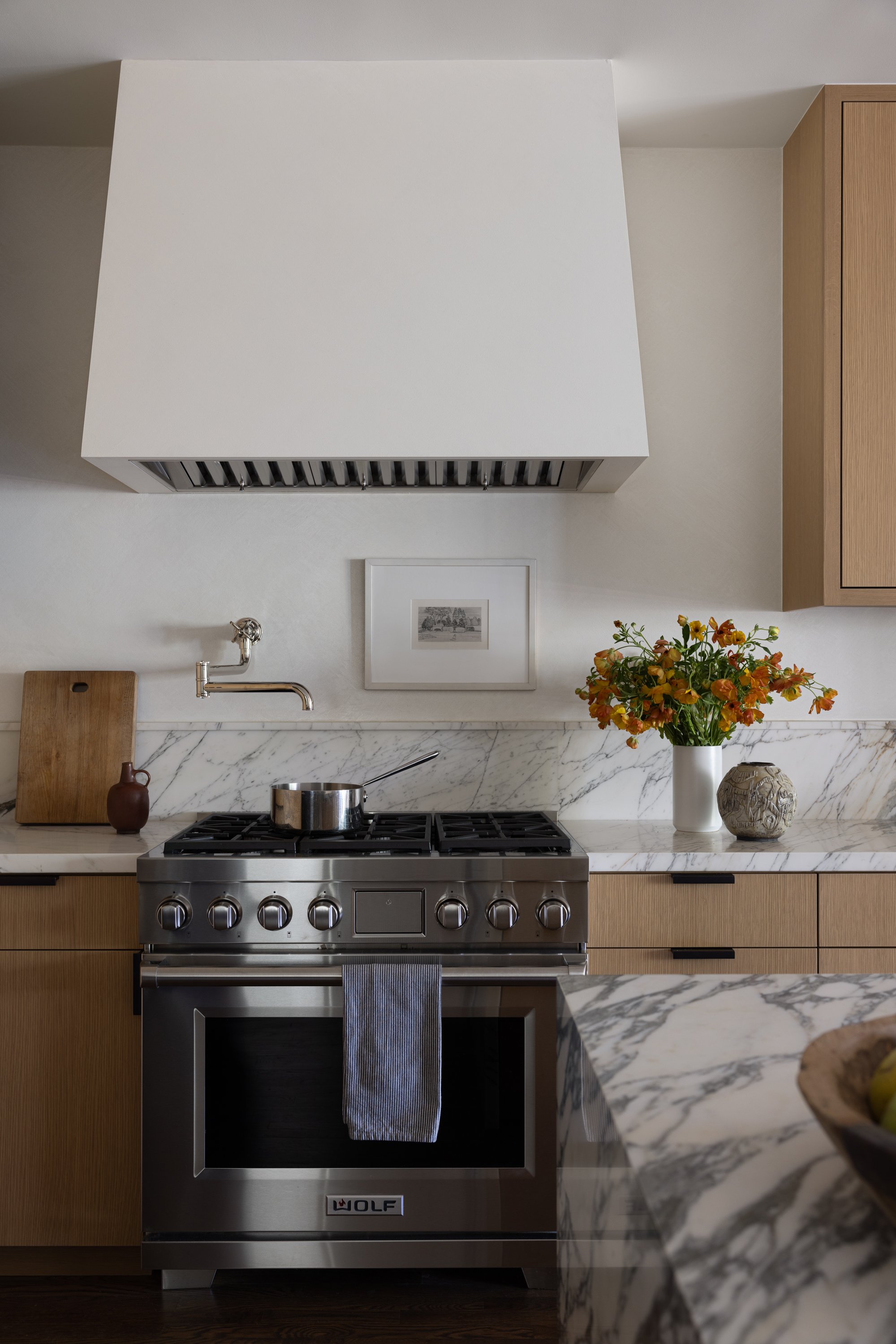 Vignette of the kitchen, showing the range with large hood and pot filler, vase with flowers.