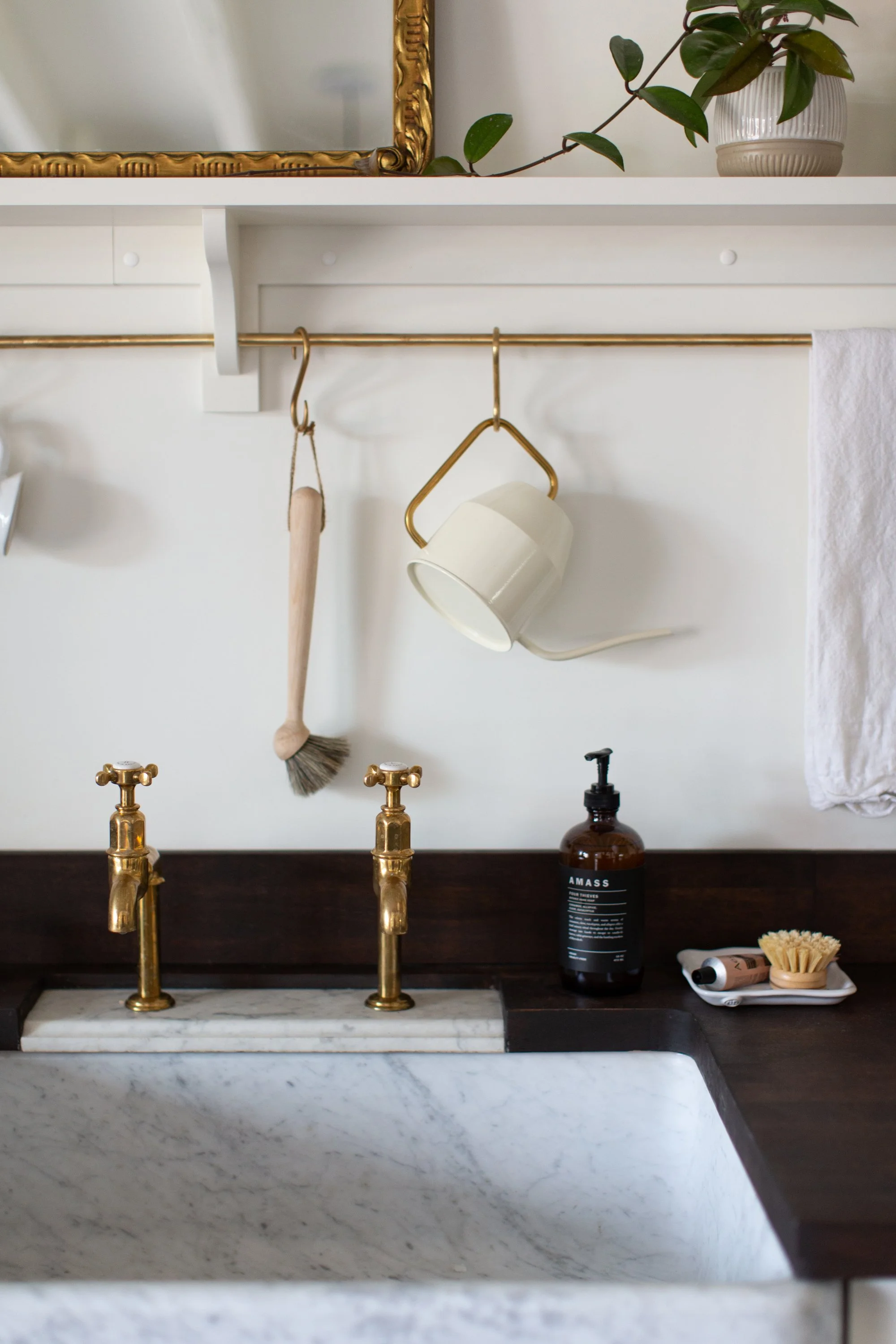 Closeup of kitchen sink with brass faucets, brass rail with natural brush, kitchen towel and watering can