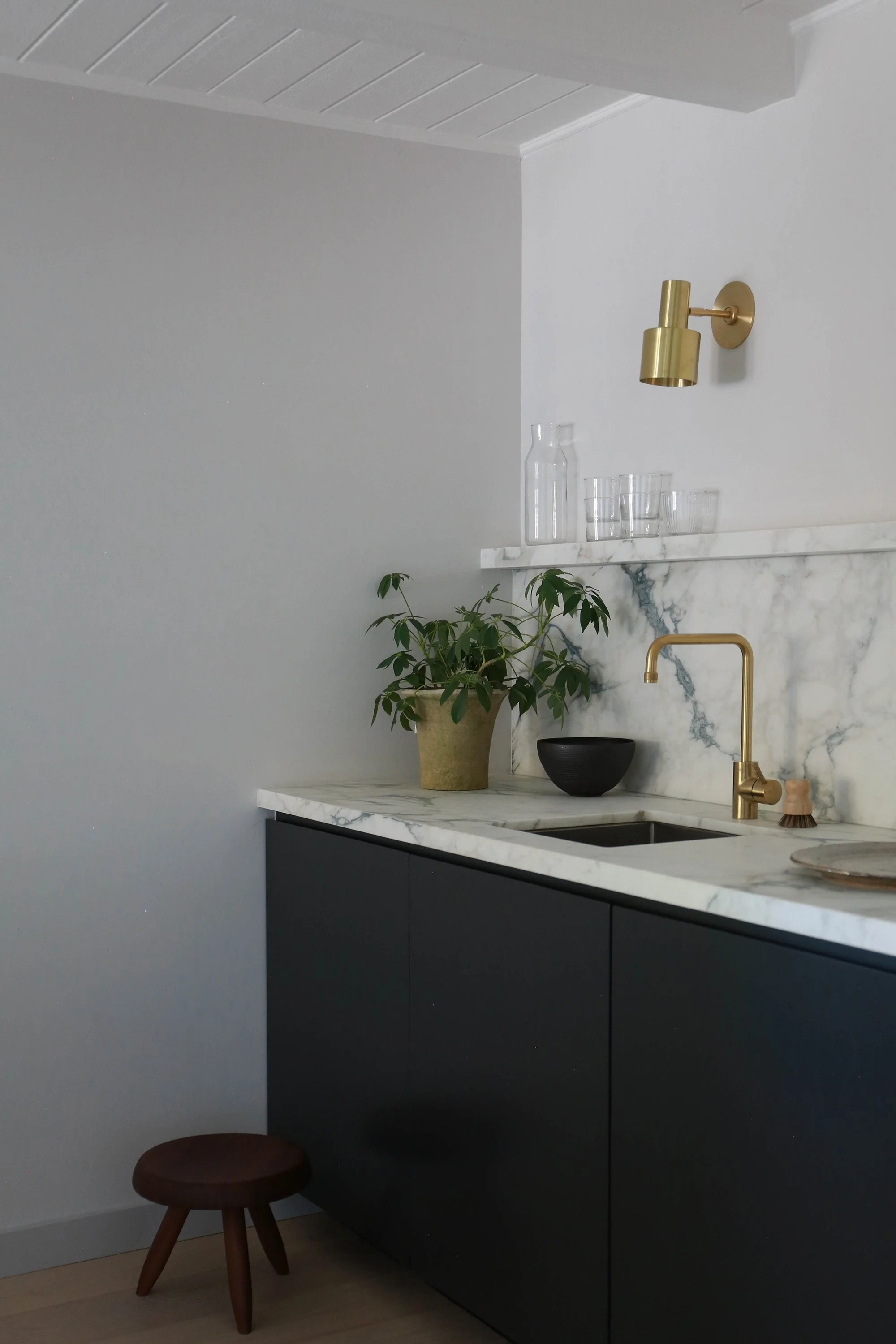 Closeup of bar, showing sink with brass faucet, glasses and planter with plant.