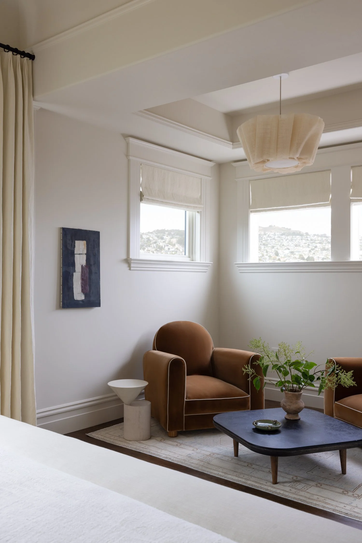 View of the seating area in the bedroom, showing two bronze brown side chairs, a dark coffee table and a vase with branches.
