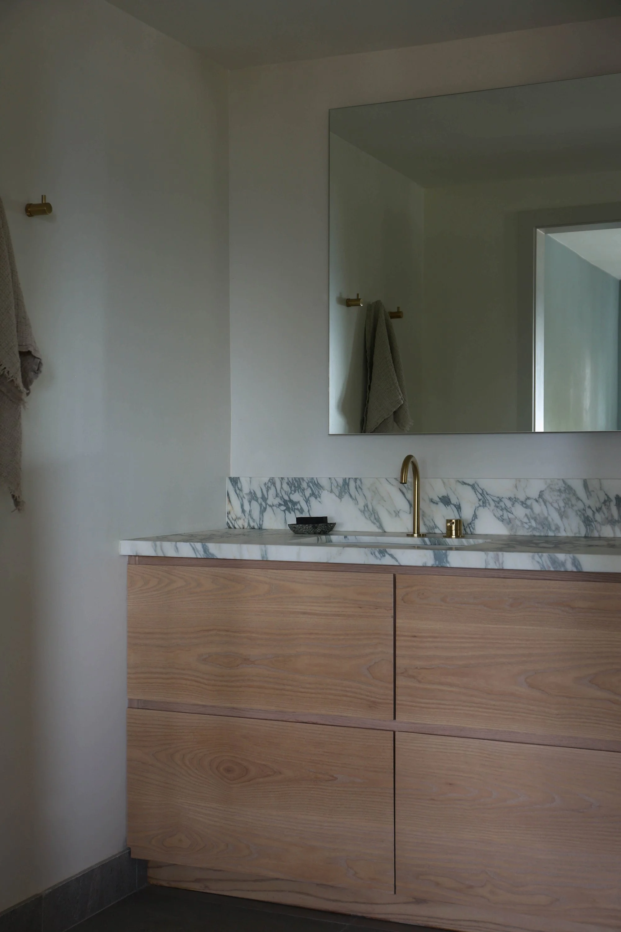 Bathroom view showing sink, cabinets, mirror and hooks with towels.