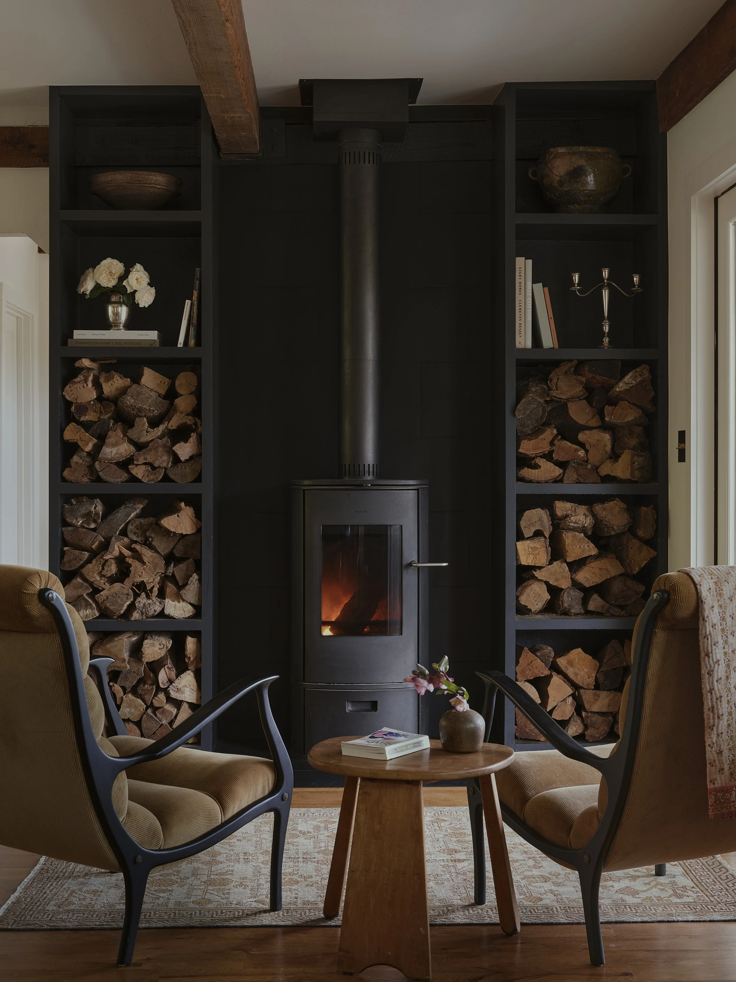 Seating in front of a fireplace with stacks of wood in bookcase.