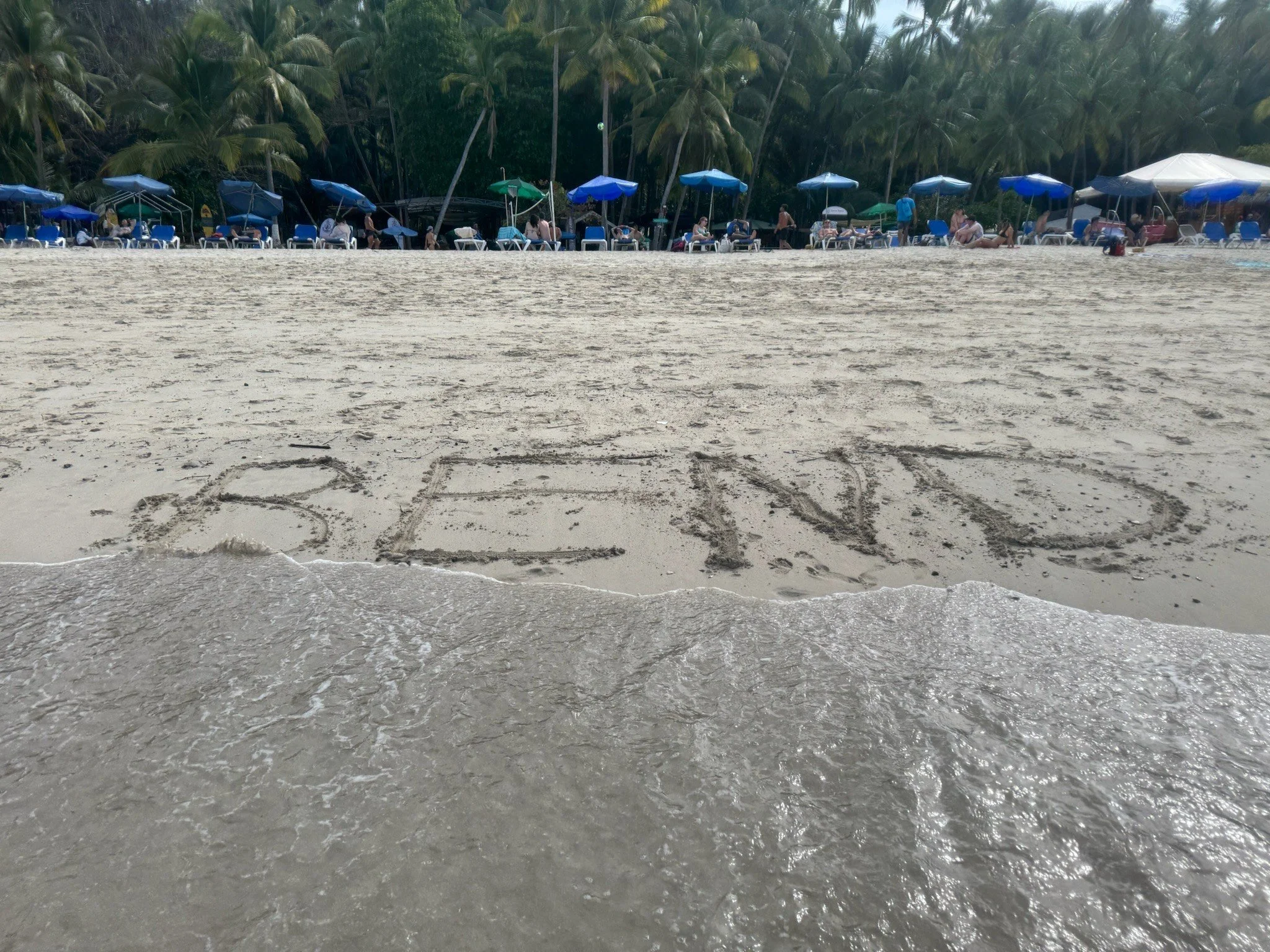 Writing in the sand on a beach spelling out 'BEACH' with waves approaching.
