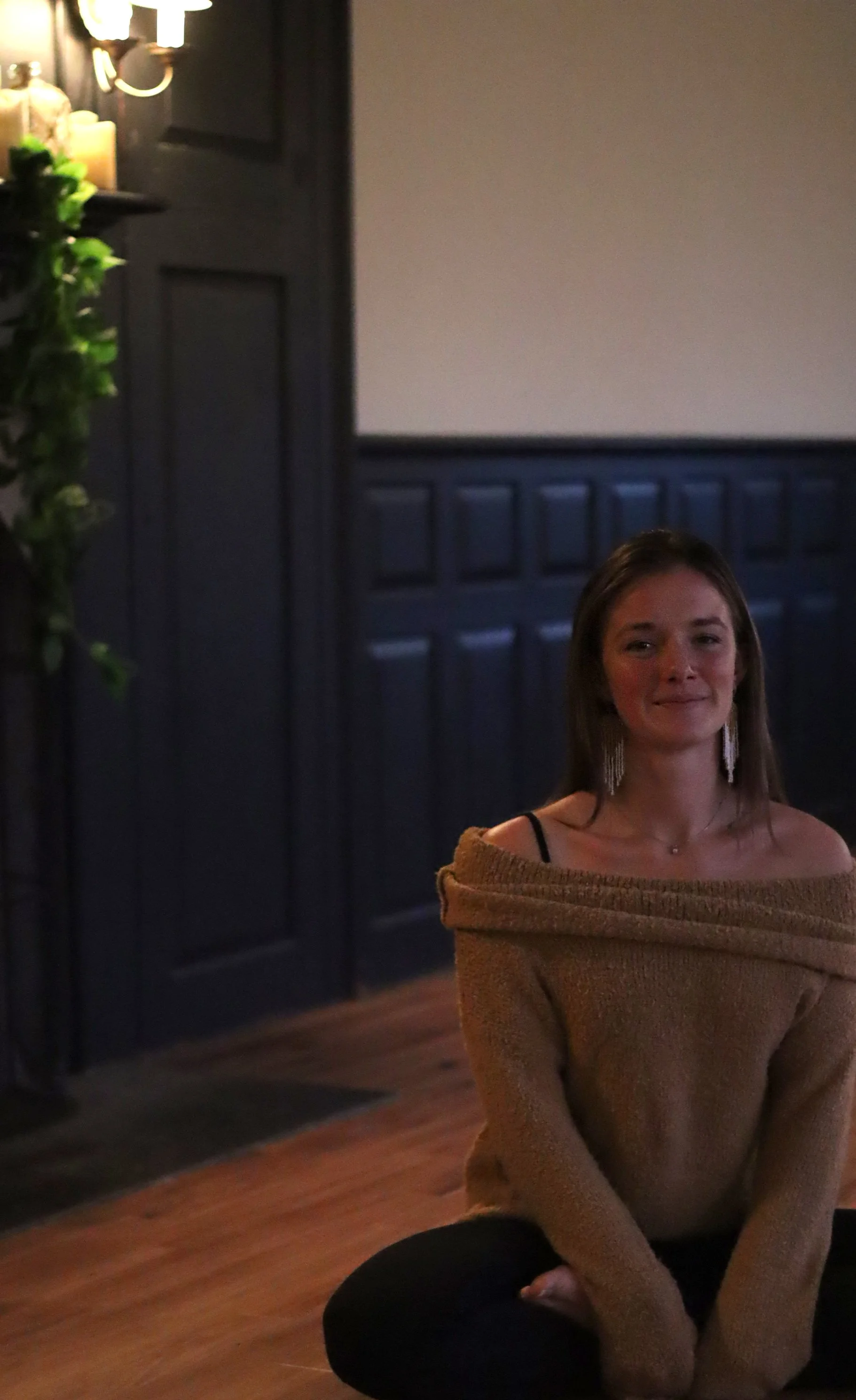 Smiling woman in black tank top and shorts standing in a field of white flowers under a blue sky with some clouds.