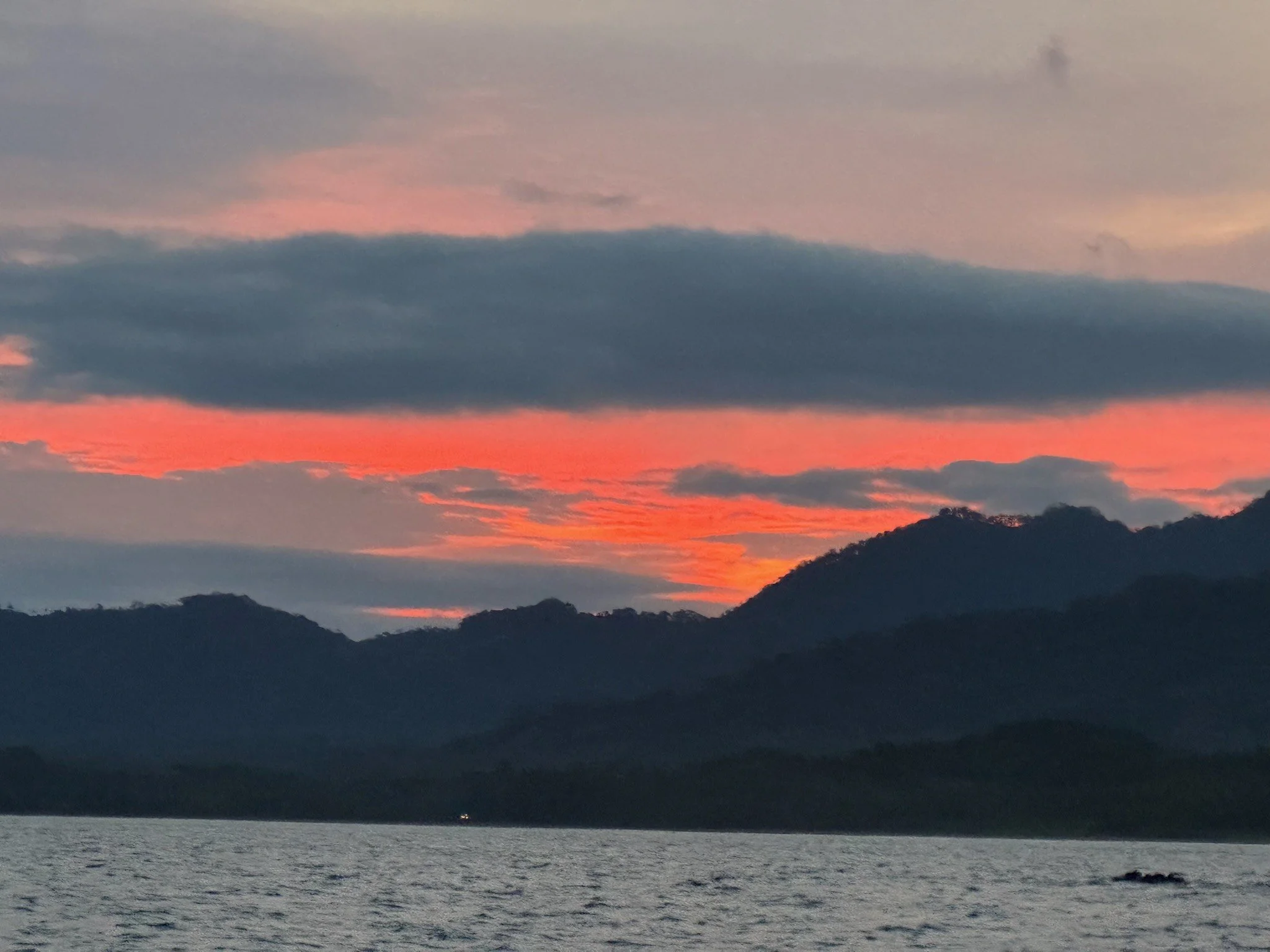 Sunset over mountains and water with pink and orange clouds in the sky.