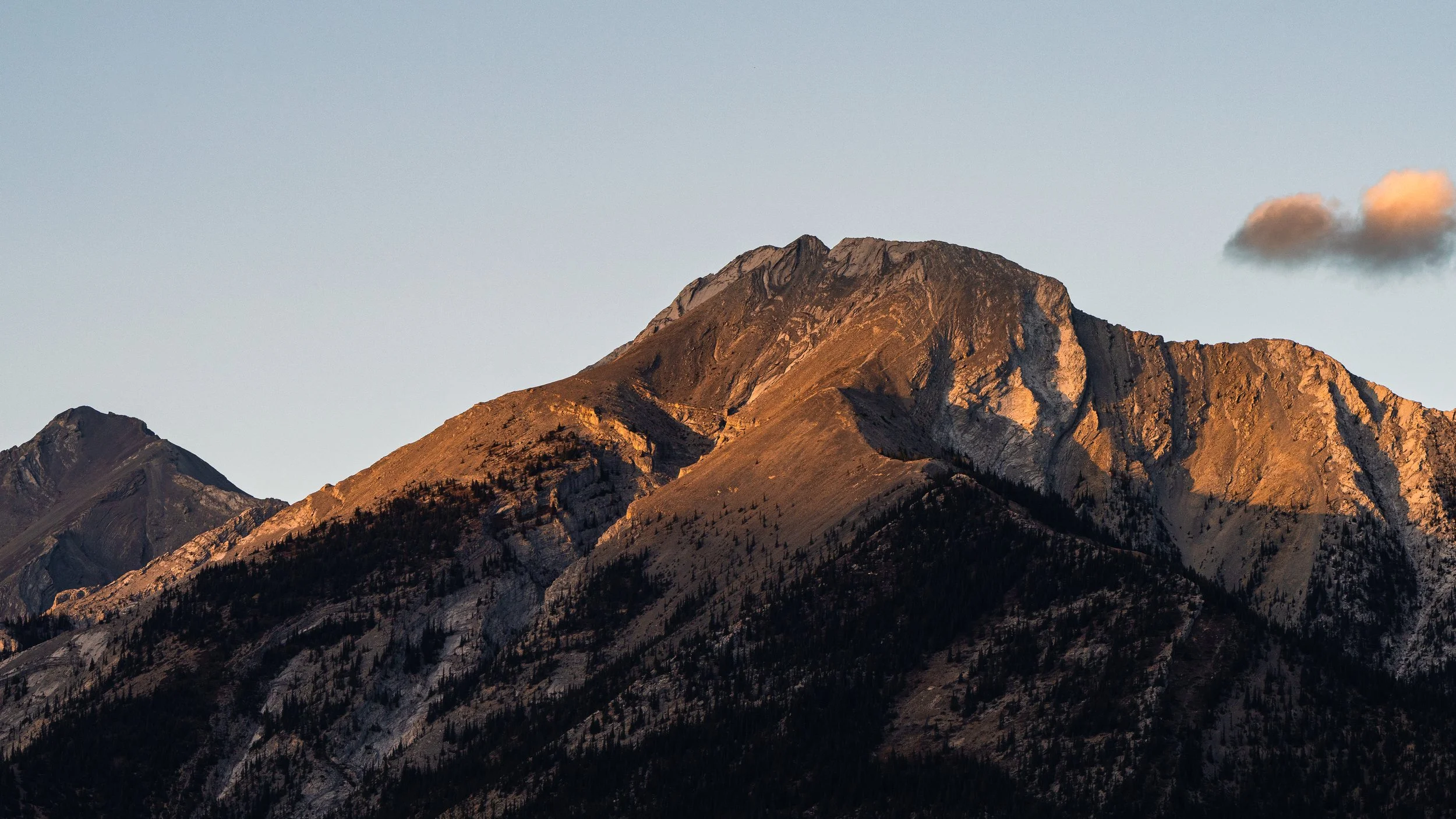 Mountain range with rocky peaks and forested slopes during sunset.