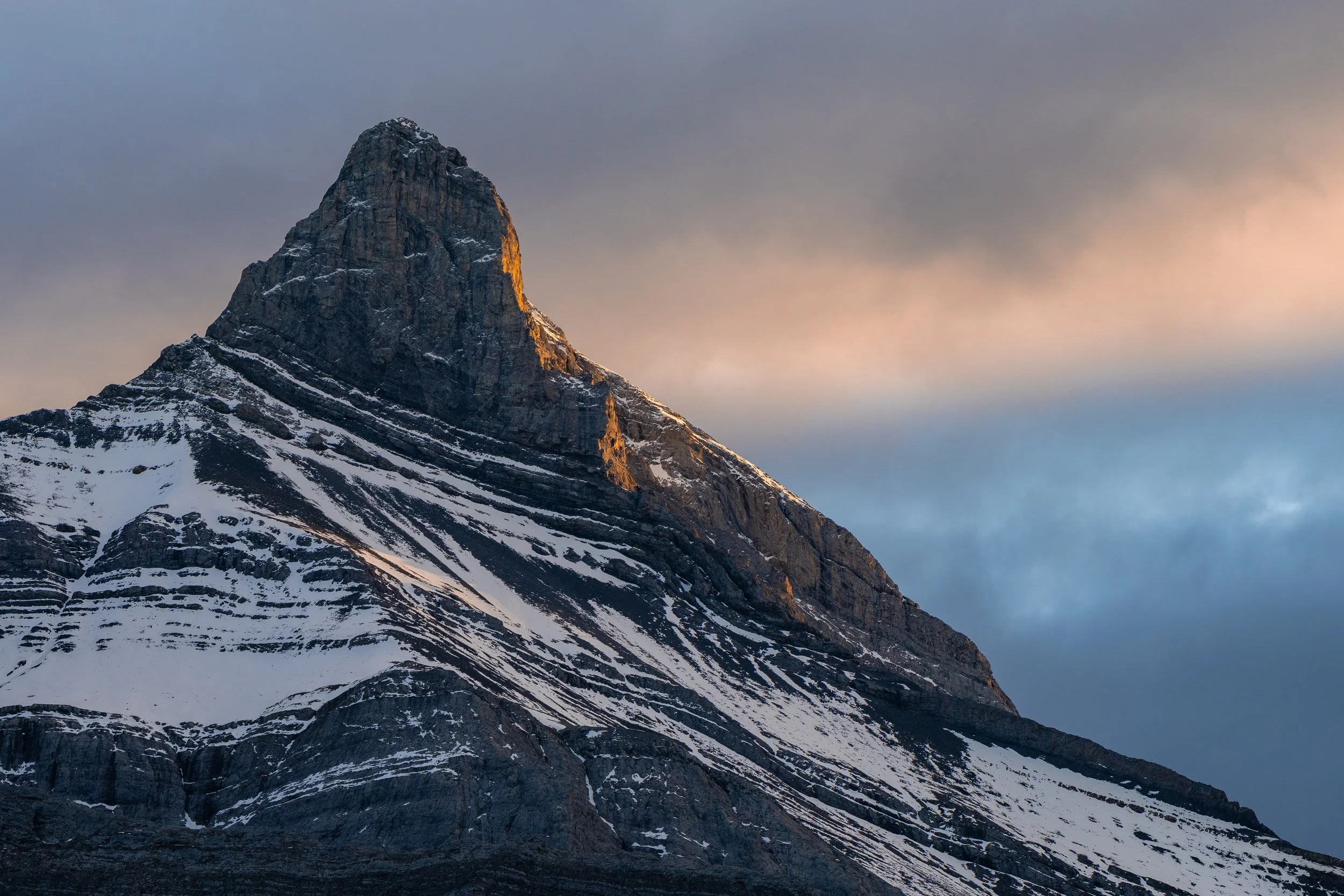 Snow-covered mountain peak under a cloudy sky during sunset.