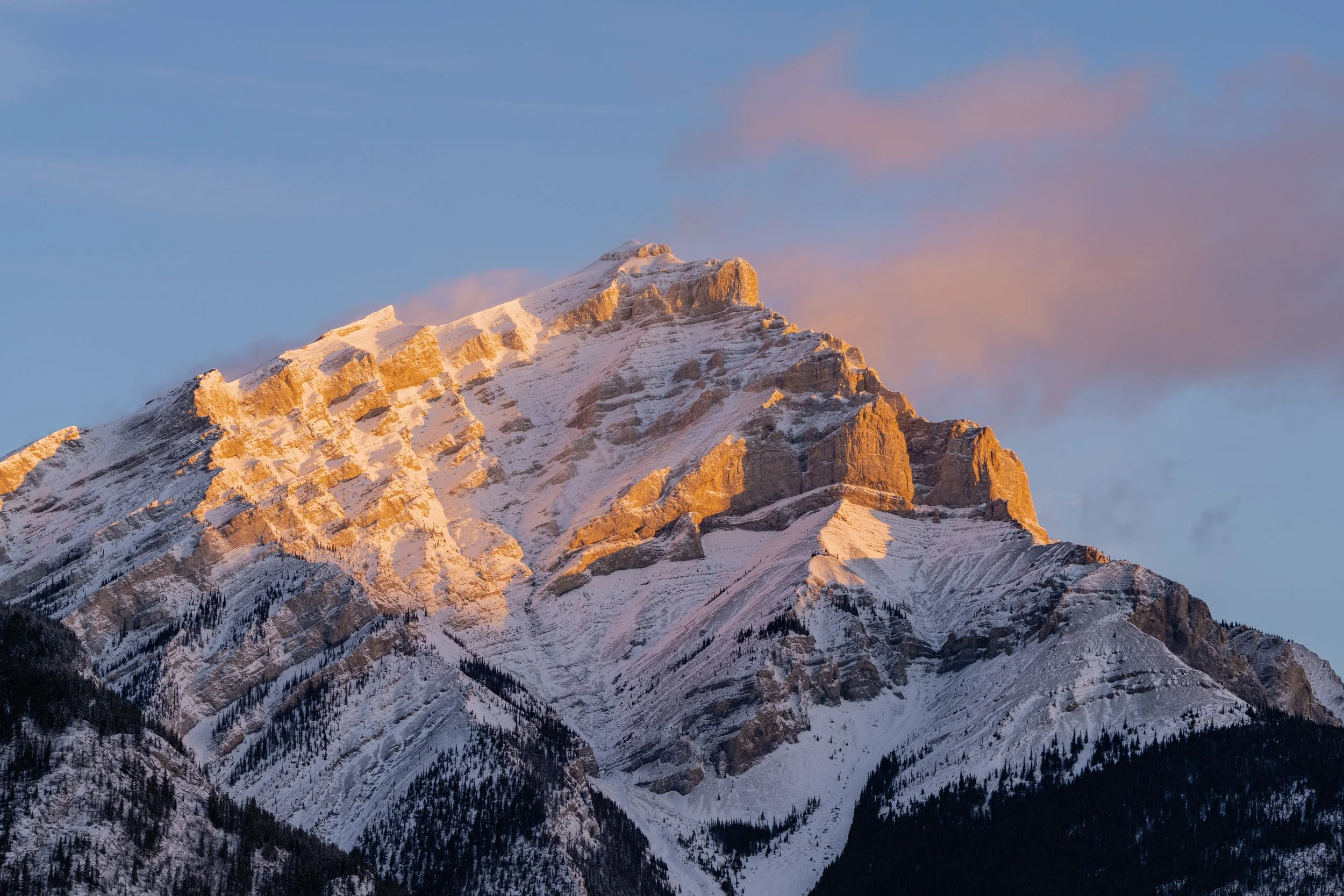 Snow-covered mountain peak at sunset with pink clouds in sky.