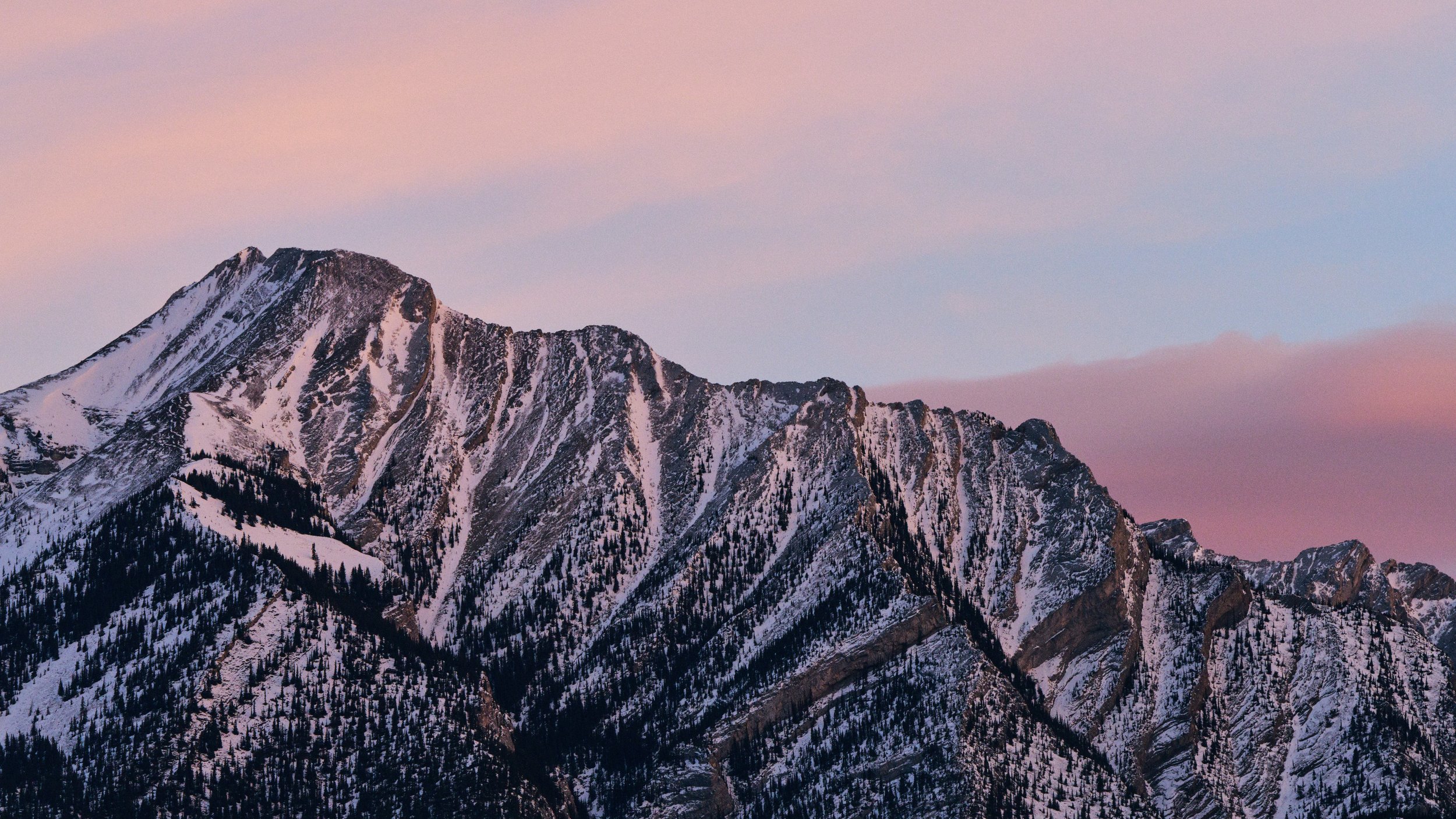 Snow-covered mountain range during sunrise with a pink and purple sky.