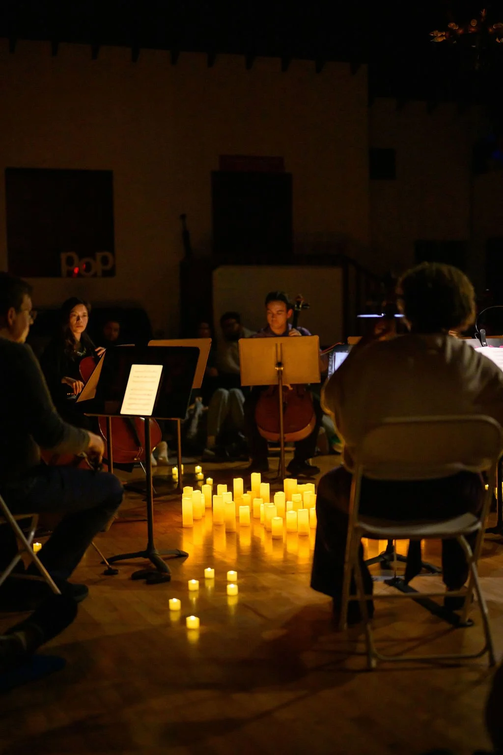 A group of musicians performing in a dimly lit indoor performance with candles on the floor.