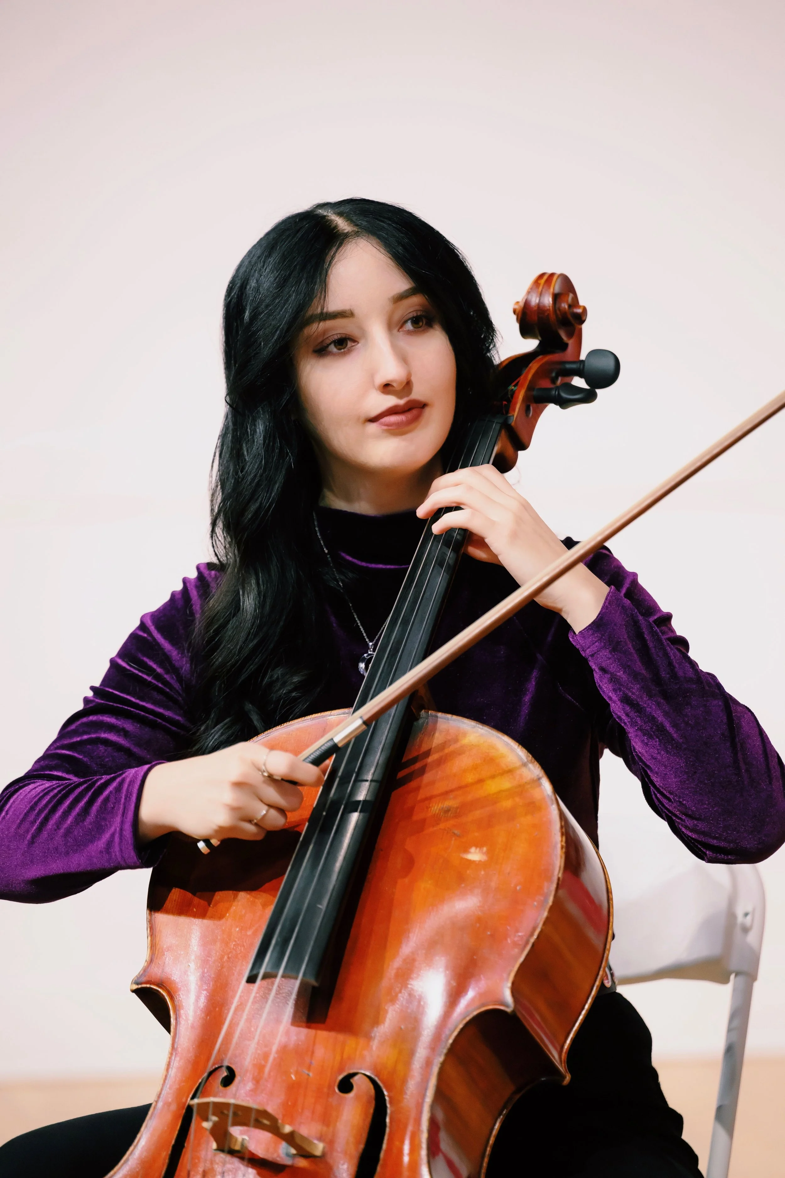 A young woman with long black hair playing a cello.