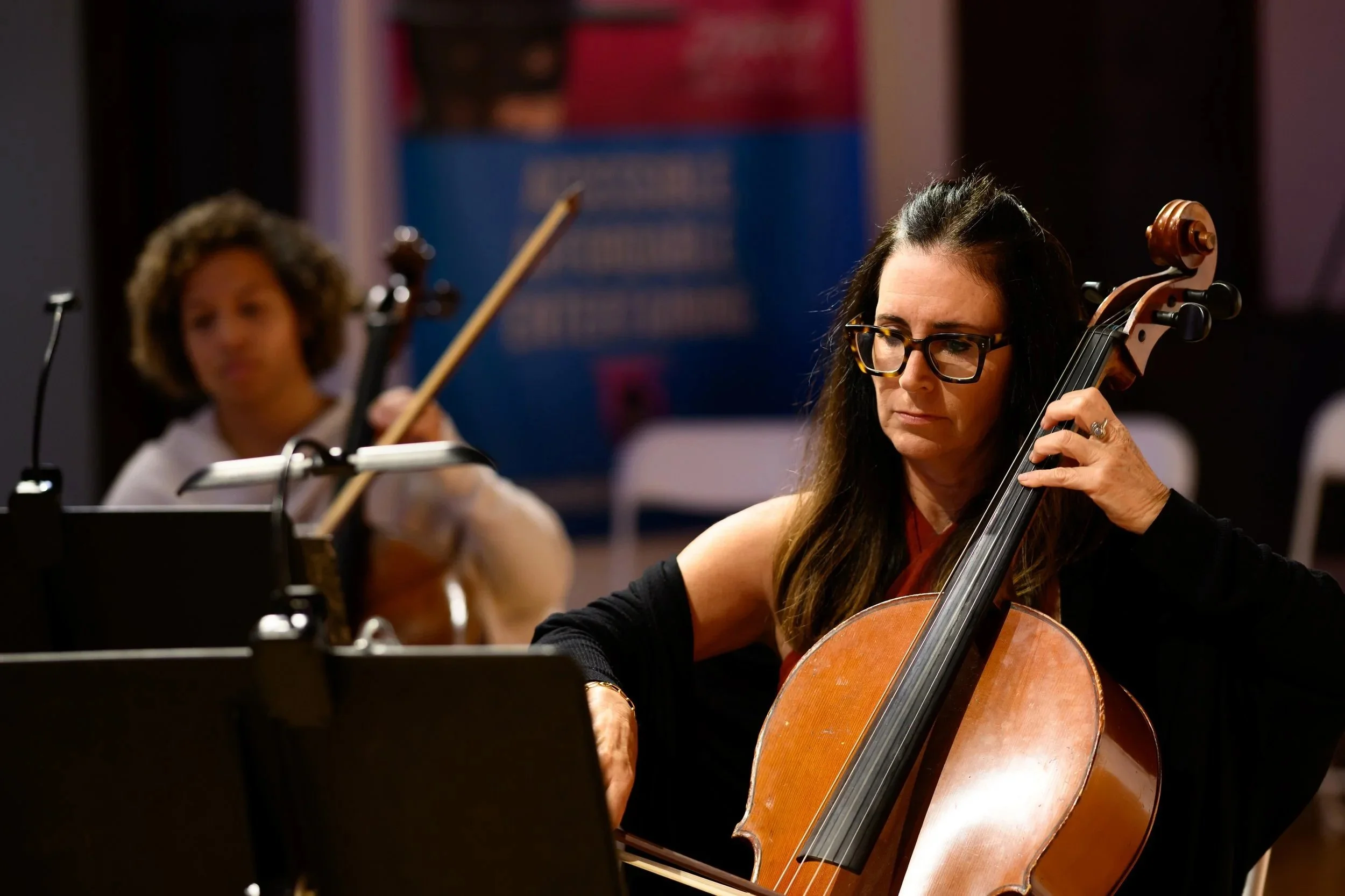 A woman with dark long hair playing the cello with a thoughtful, contemplative expression.