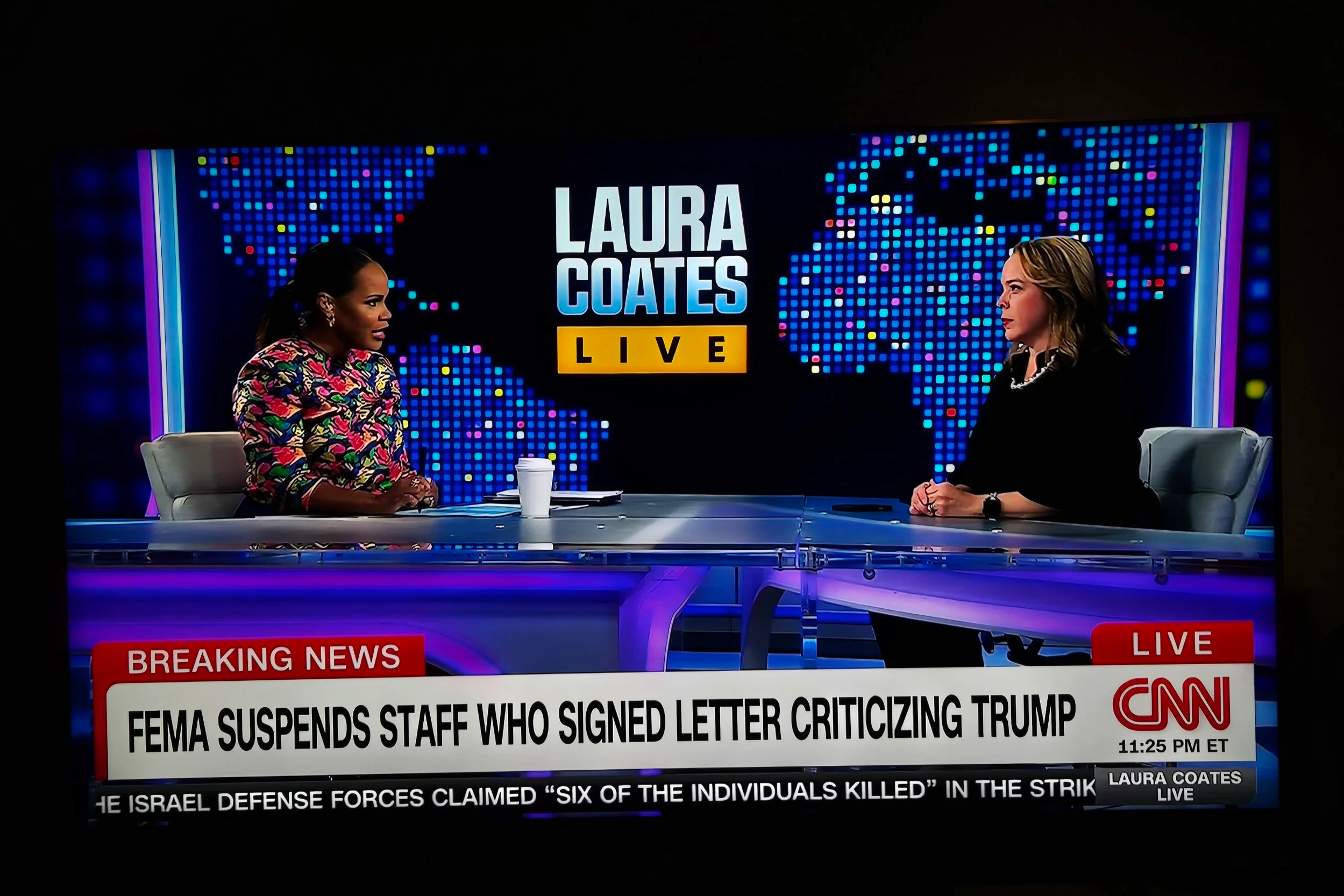 Television screen showing a news interview on CNN. Two women are seated at a news desk with a digital world map background. A banner at the bottom displays breaking news about FEMA suspending staff who signed a letter criticizing Trump. The time shown is 11:25 PM ET, and the program is Laura Coates Live.