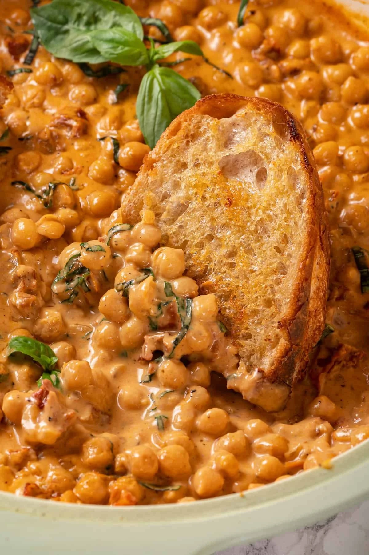 Close-up of a bowl of chickpea curry garnished with basil leaves and a toasted bread slice.