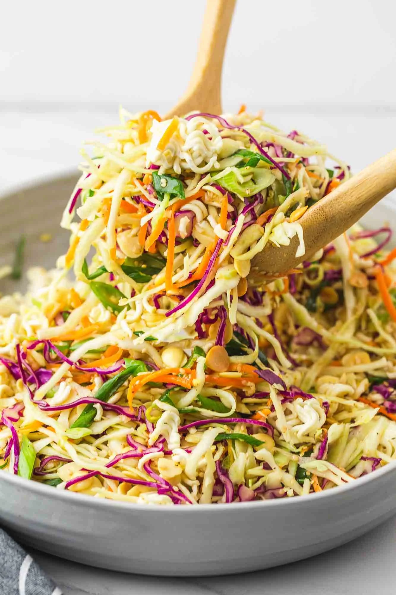 Close-up of a colorful bowl of shredded vegetable salad with carrots, cabbage, and green onions, with wooden salad servers.