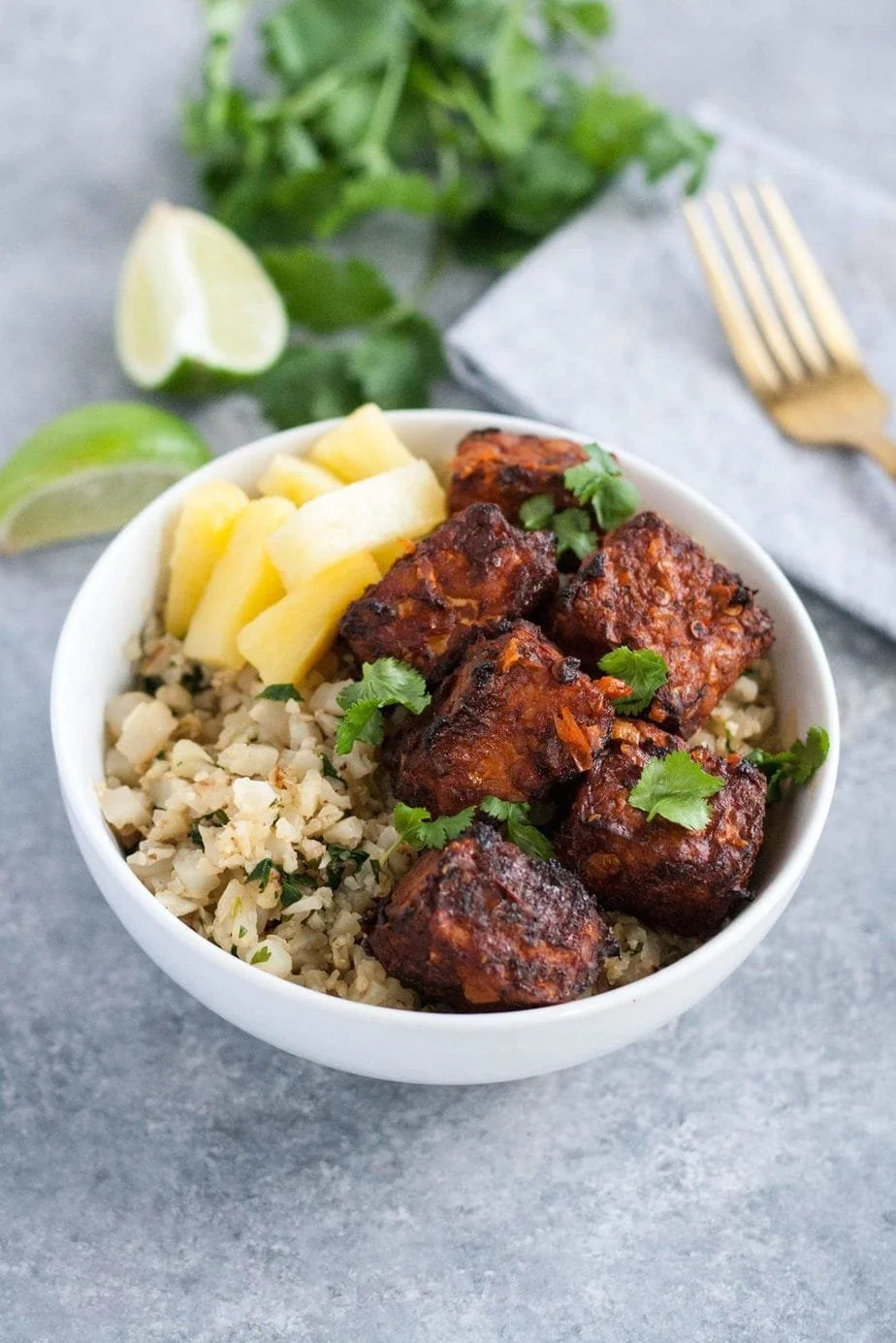 Bowl of rice with vegan meatballs, pineapple chunks, and garnished with cilantro, with lime wedges in the background.