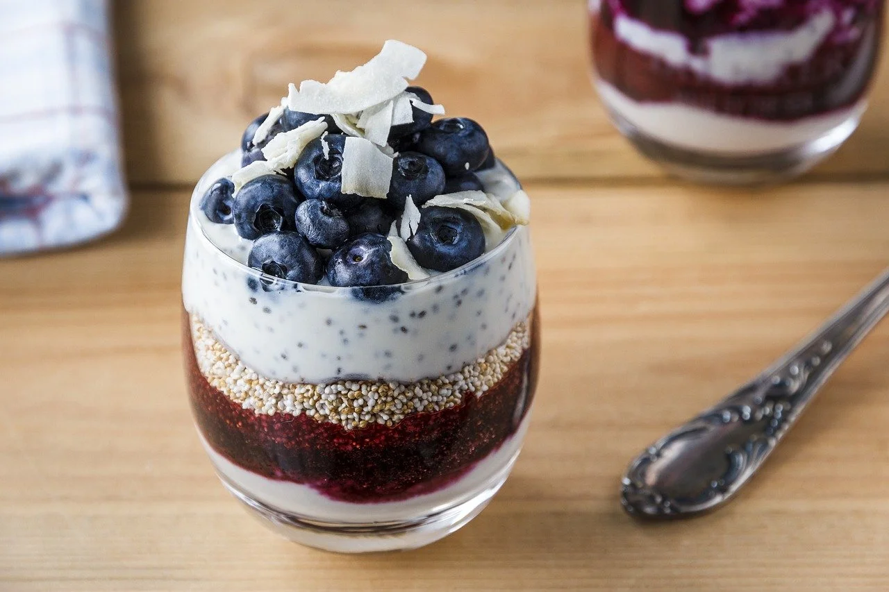 A layered blueberry parfait in a glass with blueberries on top, white chocolate shavings, and various layers of yogurt, granola, and berry compote.