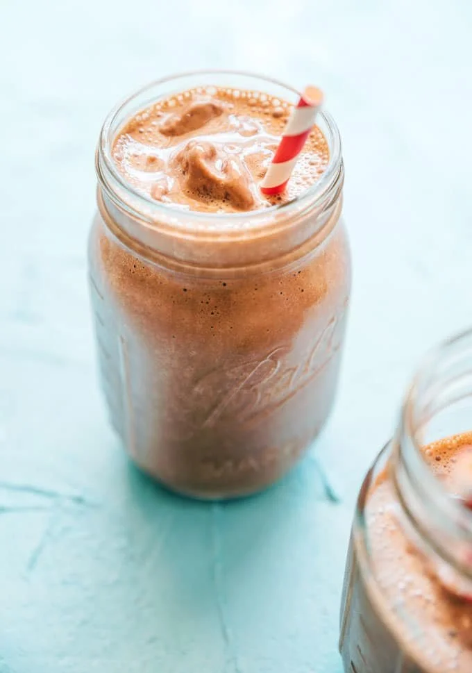 Vegan Chocolate milkshake in a glass jar with a striped paper straw on a light blue surface.