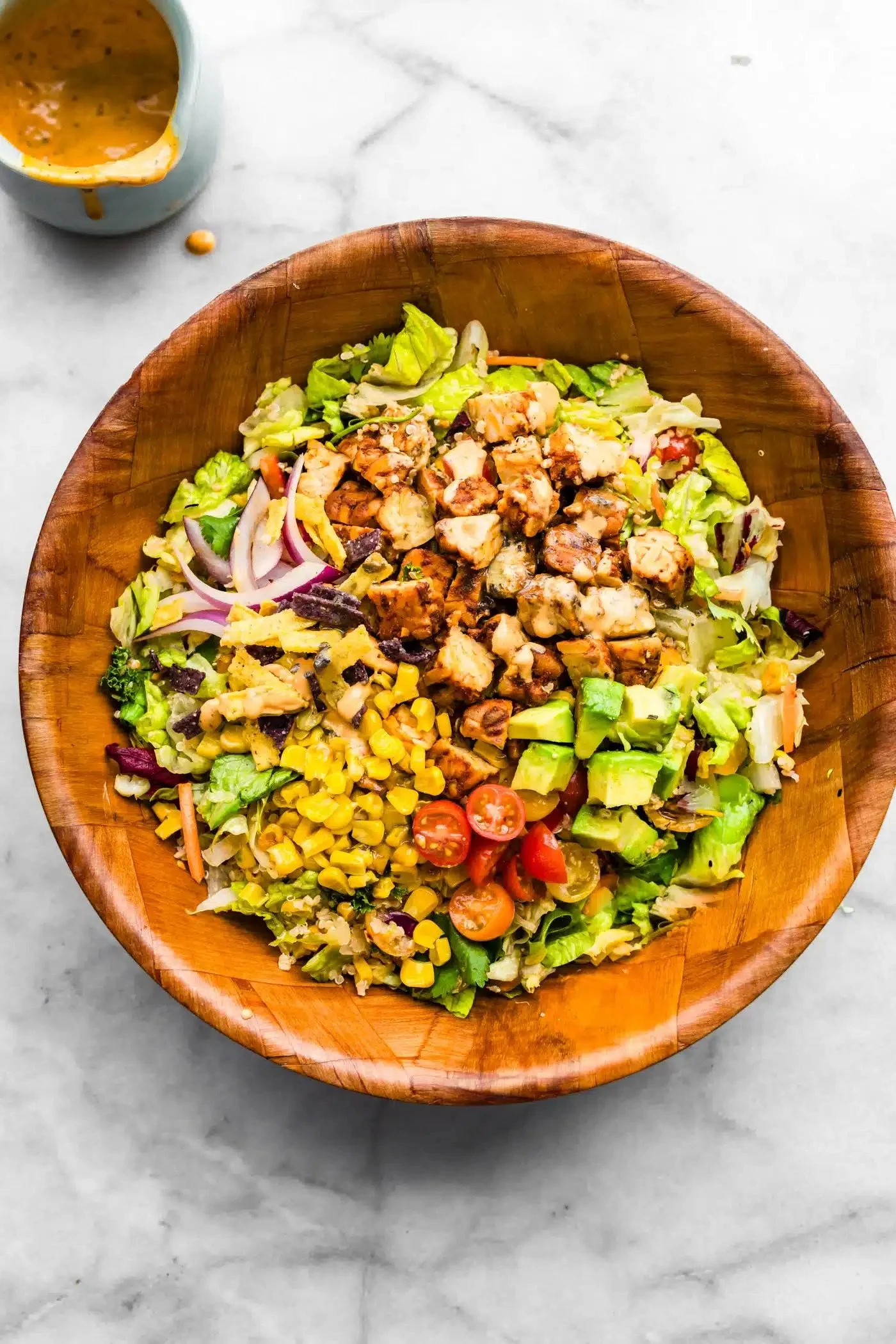 Mixed salad in a wooden bowl with grilled chicken, cherry tomatoes, sliced onions, avocado, corn, lettuce, and other vegetables.