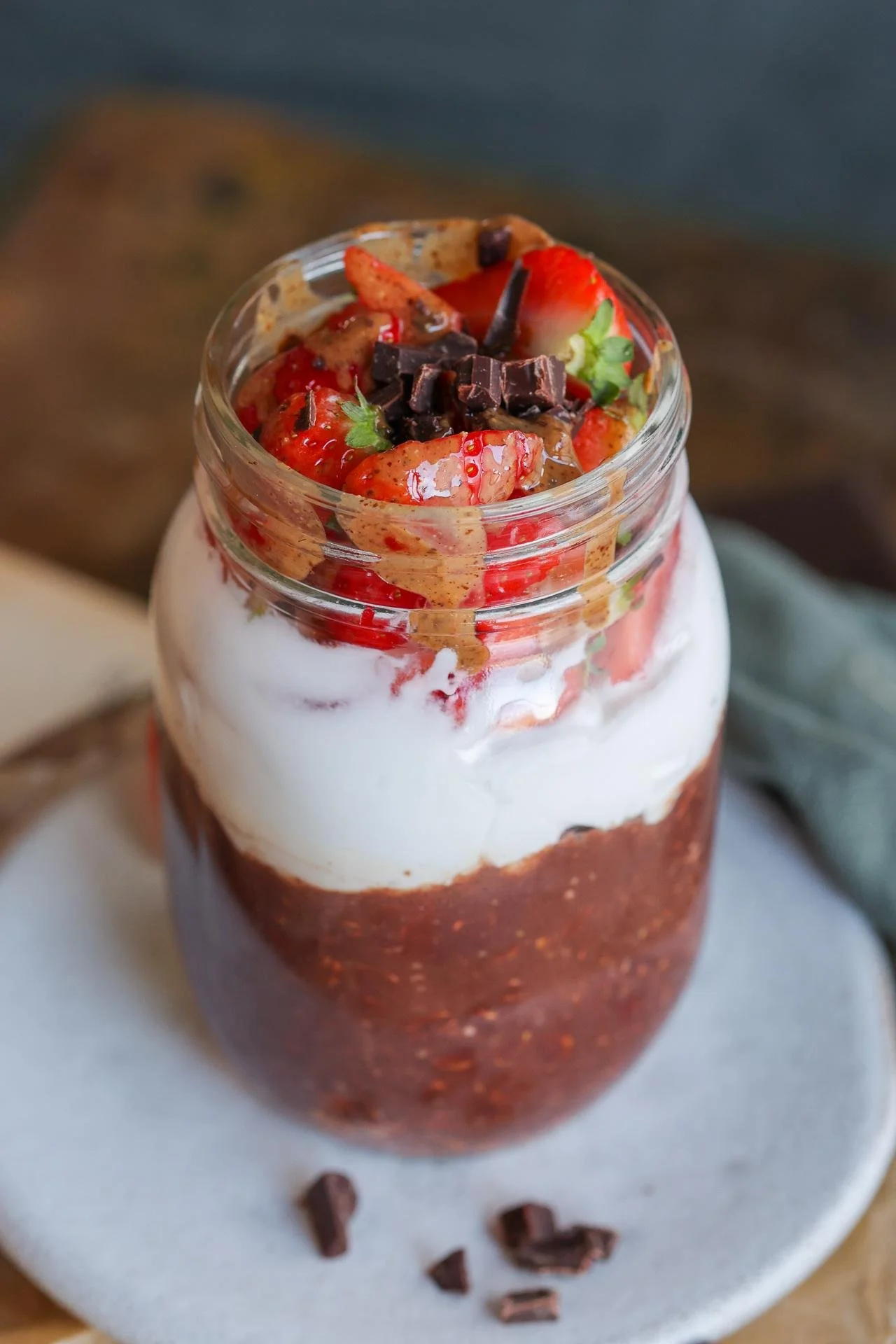 Vegan Strawberry chocolate layered dessert in a glass jar with strawberries, whipped cream, and chocolate pieces on top.