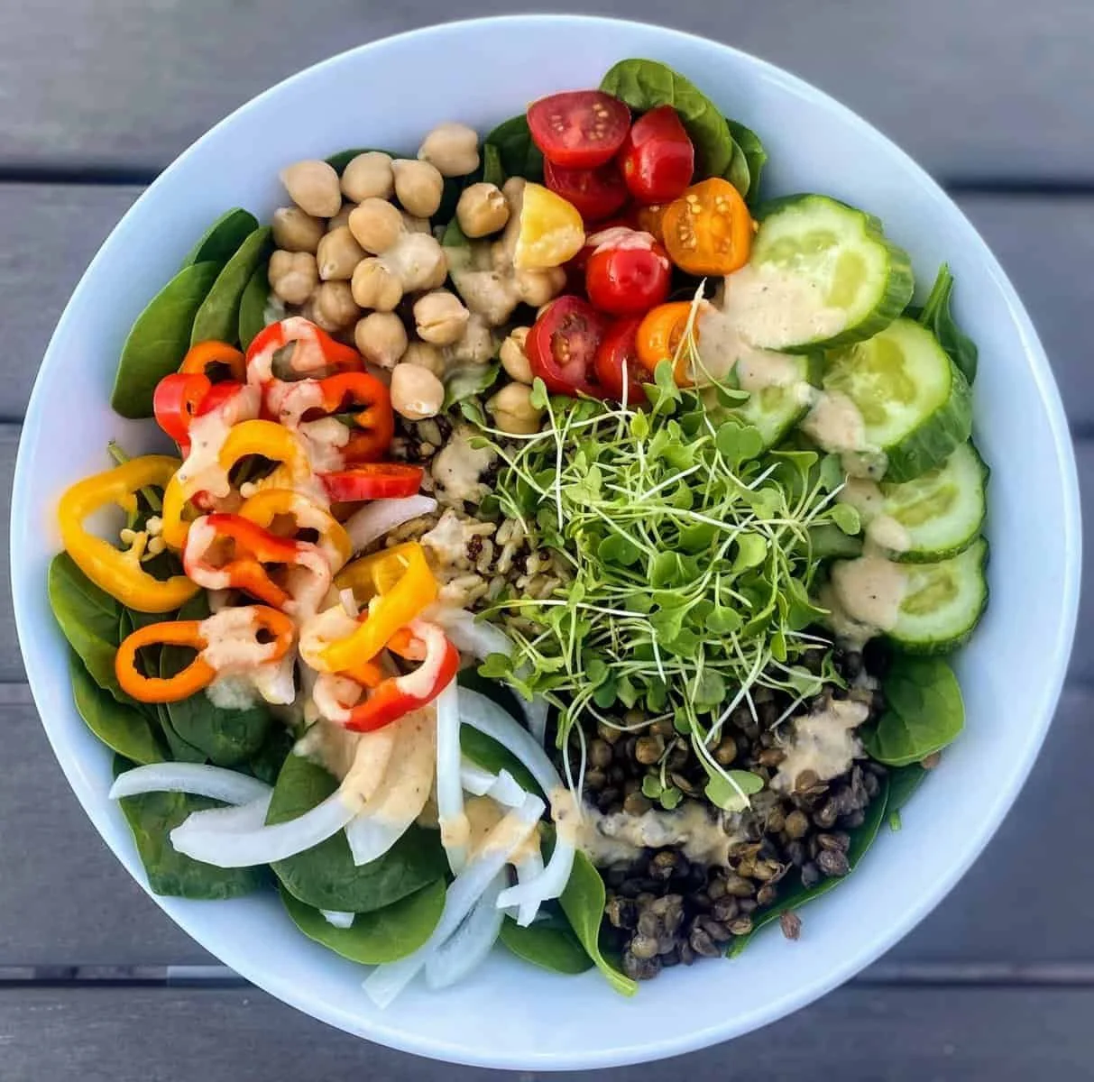 A bowl of fresh salad with cucumber slices, cherry tomatoes, chickpeas, microgreens, bell peppers, onions, and leafy greens.