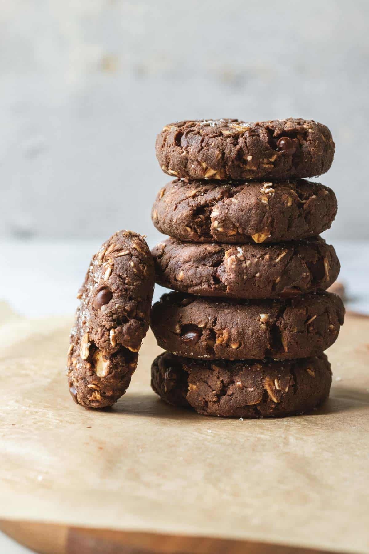 Stack of five chocolate cookies with chopped nuts and chocolate chips, one cookie leaning against the stack.
