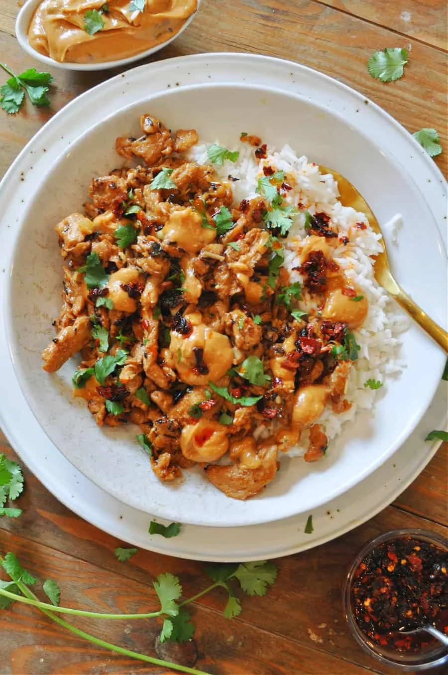 Plate of rice and tofu dish garnished with cilantro, with a side bowl of chili sauce on a wooden table.