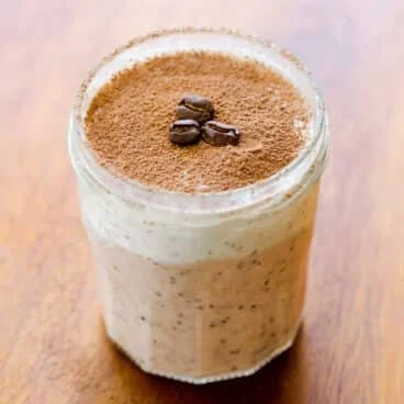A glass of coffee-flavored beverage topped with cocoa powder and coffee beans