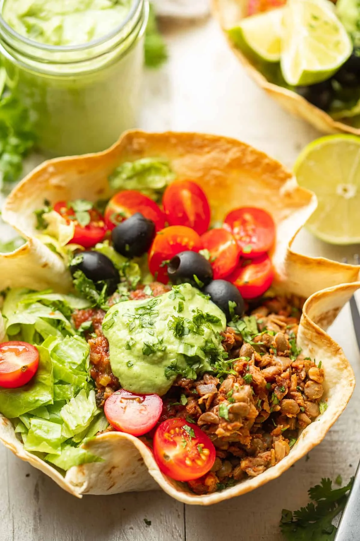 Taco salad in a tortilla bowl with cherry tomatoes, black olives, lettuce, ground meat, and guacamole.