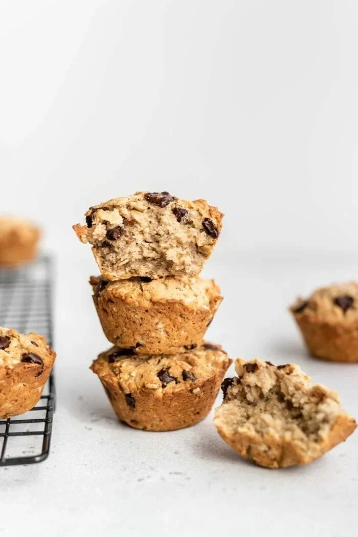 Stacked chocolate chip cookies and a broken cookie on a white surface, with a cooling rack in the background.