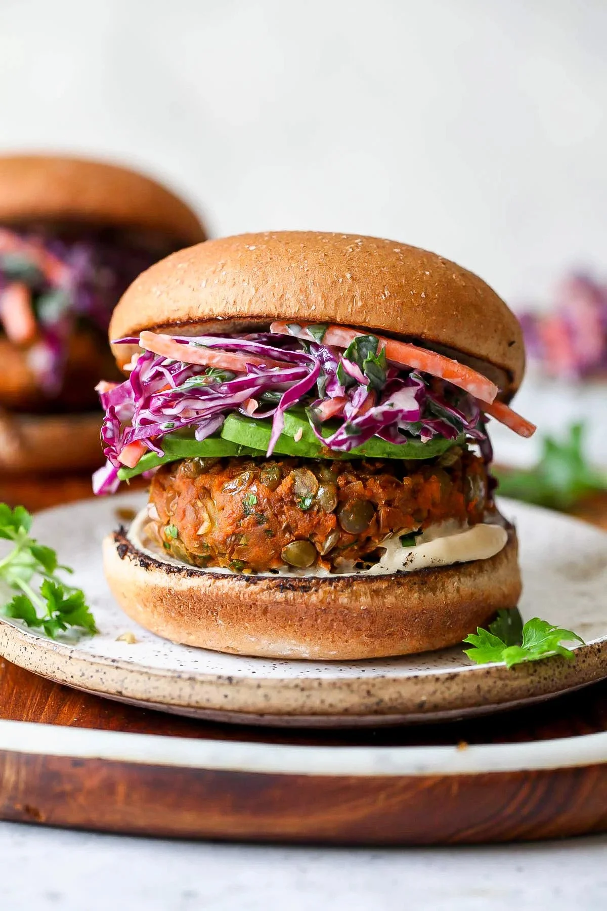 A vegan burger with a veggie patty, coleslaw, avocado, and sauce in a toasted bun on a ceramic plate.