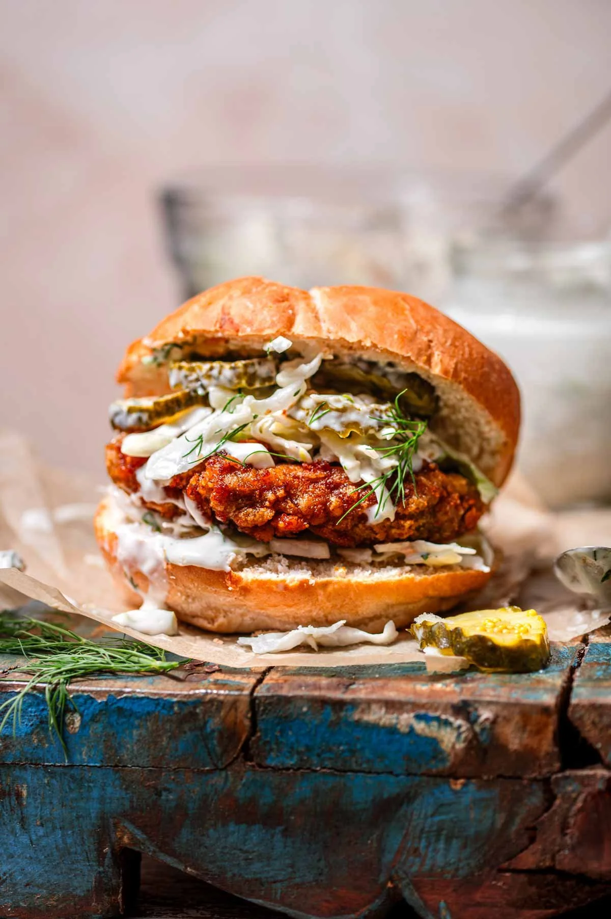 Close-up of a vegan fried chicken sandwich with coleslaw and pickles on a bun, served on a rustic wooden surface from blog Thank You Berry Much.